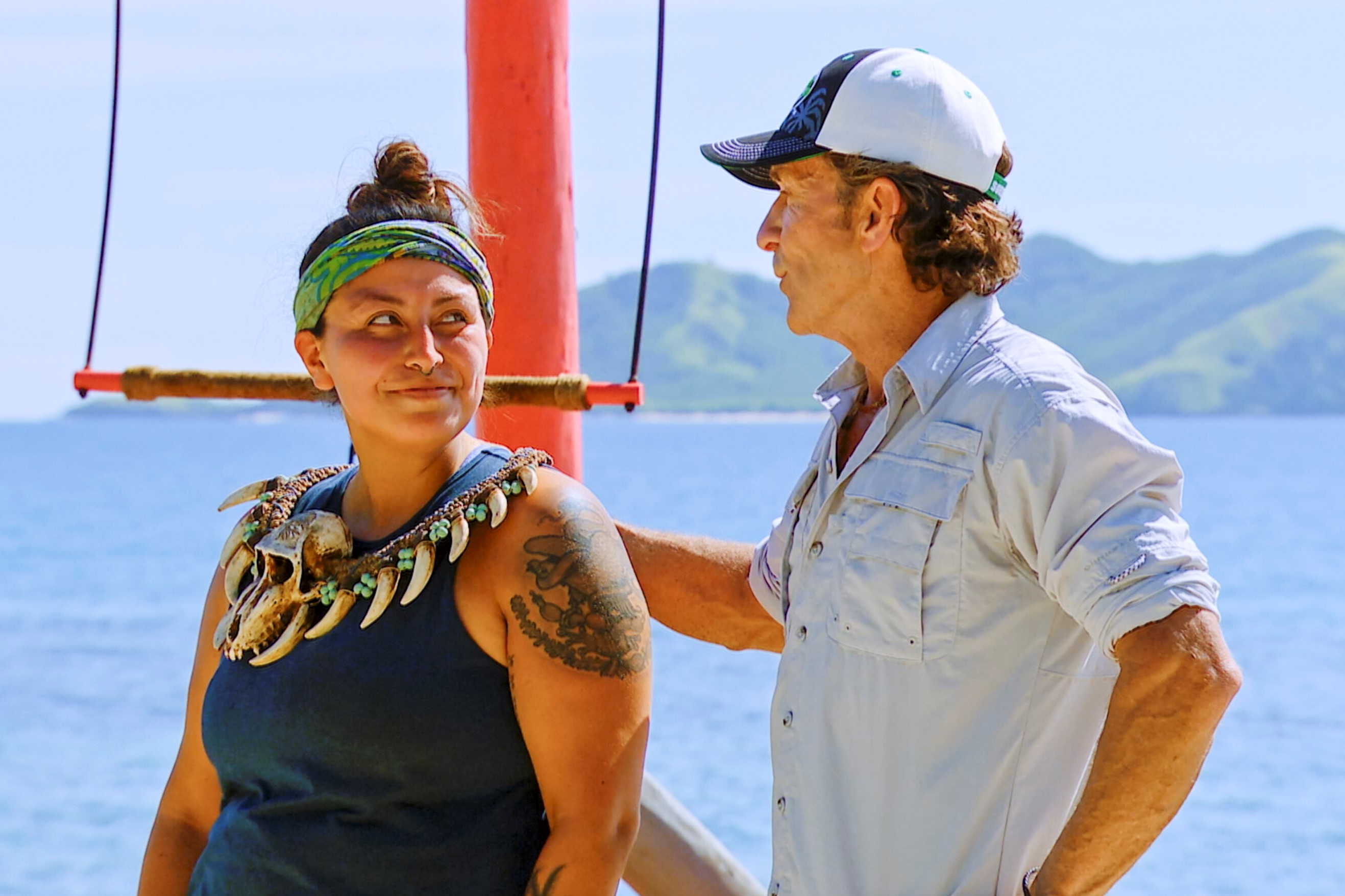 Karla Cruz Godoy and Jeff Probst, who star in 'Survivor' Season 43 on CBS, which has very few spoilers, appear in a episode. Jeff gives Karla the immunity necklace after she wins a challenge. Karla wears a dark blue tank top, the immunity necklace, and her green and blue 'Survivor' buff. Jeff wears a light gray button-up shirt with rolled-up sleeves and a black and white 'Survivor' baseball cap.