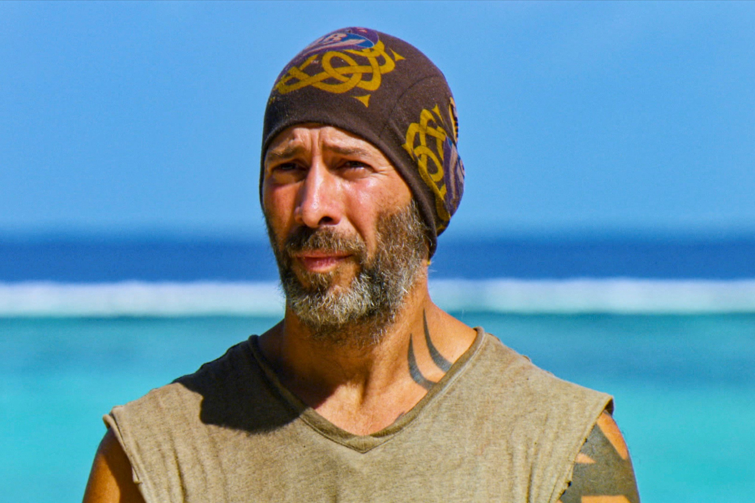 Tony Vlachos, who is a two-time 'Survivor' winner, wears a sleeveless gray shirt and brown and gold 'Survivor: Winners at War' buff.