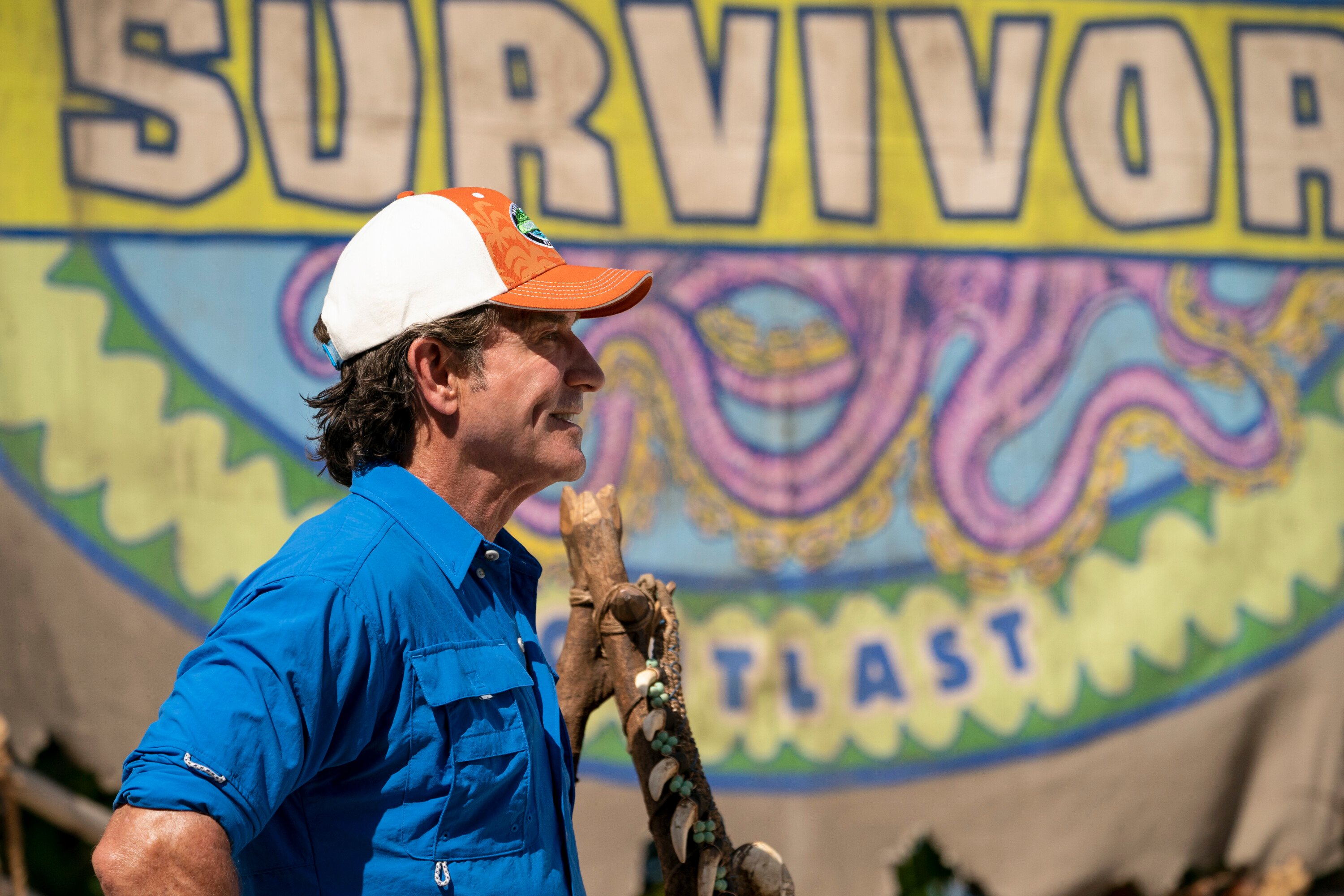 Jeff Probst, the host of 'Survivor' Season 43 on CBS, wears a blue button-up shirt and white and orange 'Survivor' baseball cap.