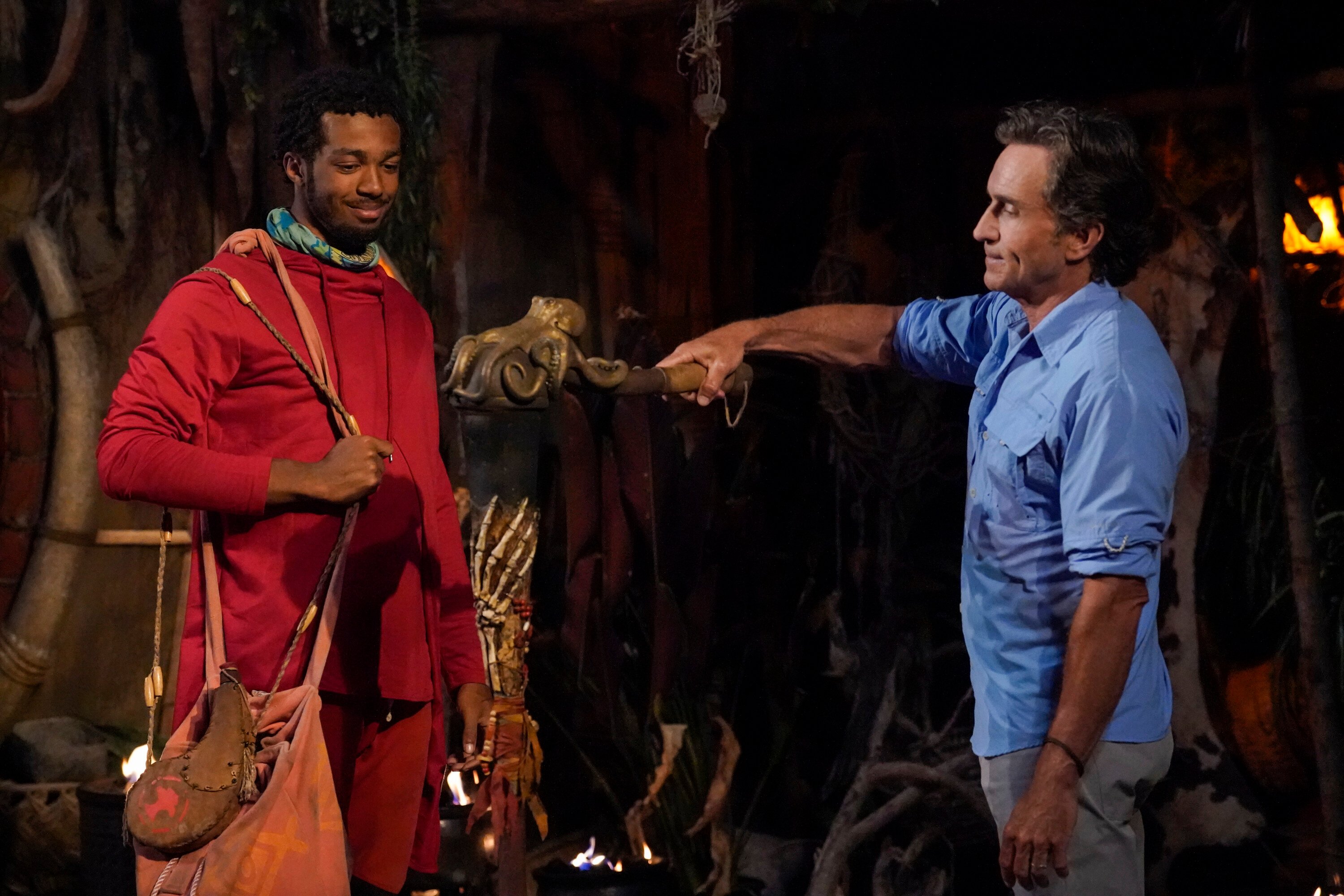 Jeff Probst snuffs Dwight Moore's torch, who had one of the immunity idols in his pocket, in 'Survivor' Season 43 Episode 7. Dwight wears a red hoodie and red shorts. Jeff wears a blue button-up shirt and gray pants.