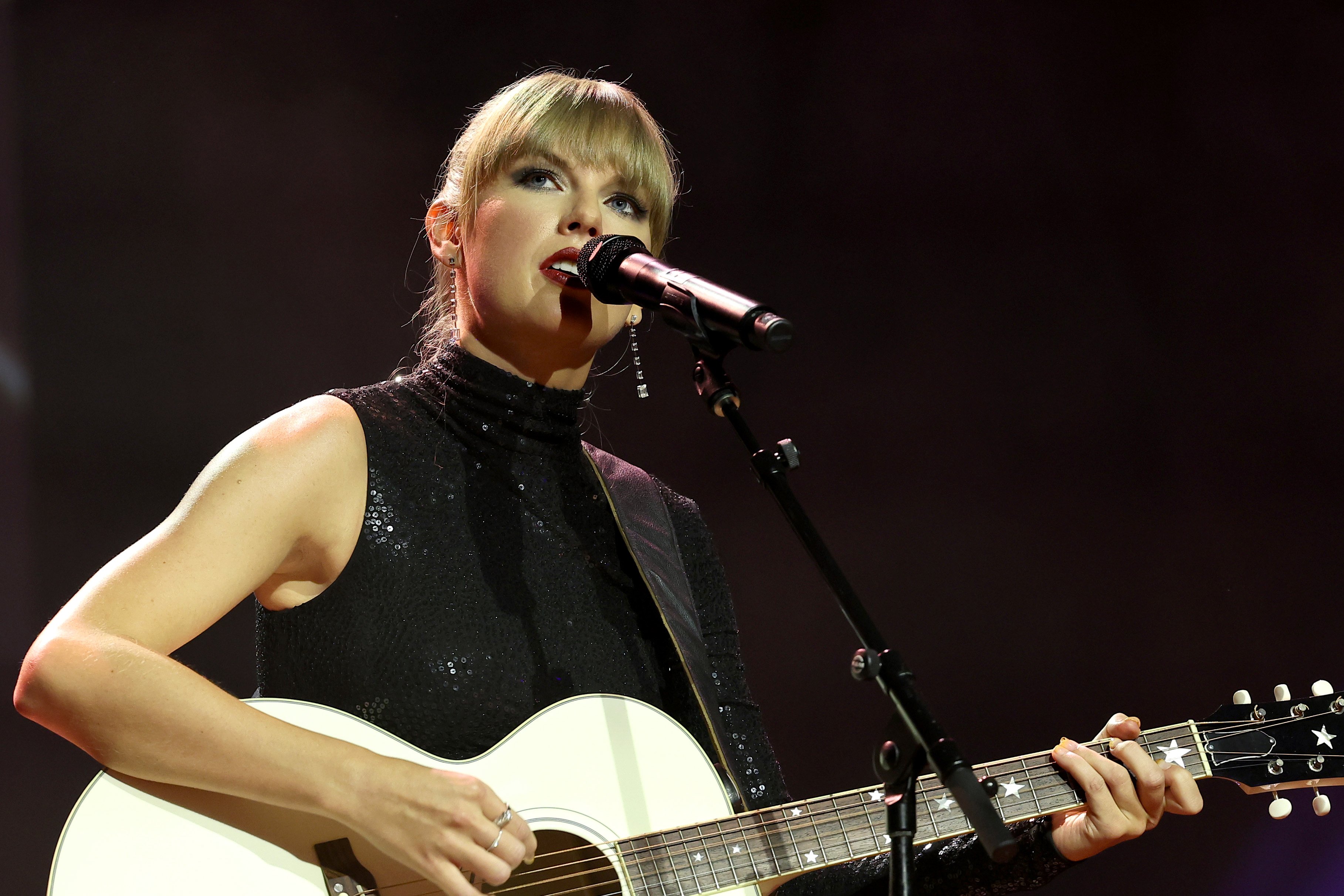 Taylor Swift performs on stage with a white acoustic guitar