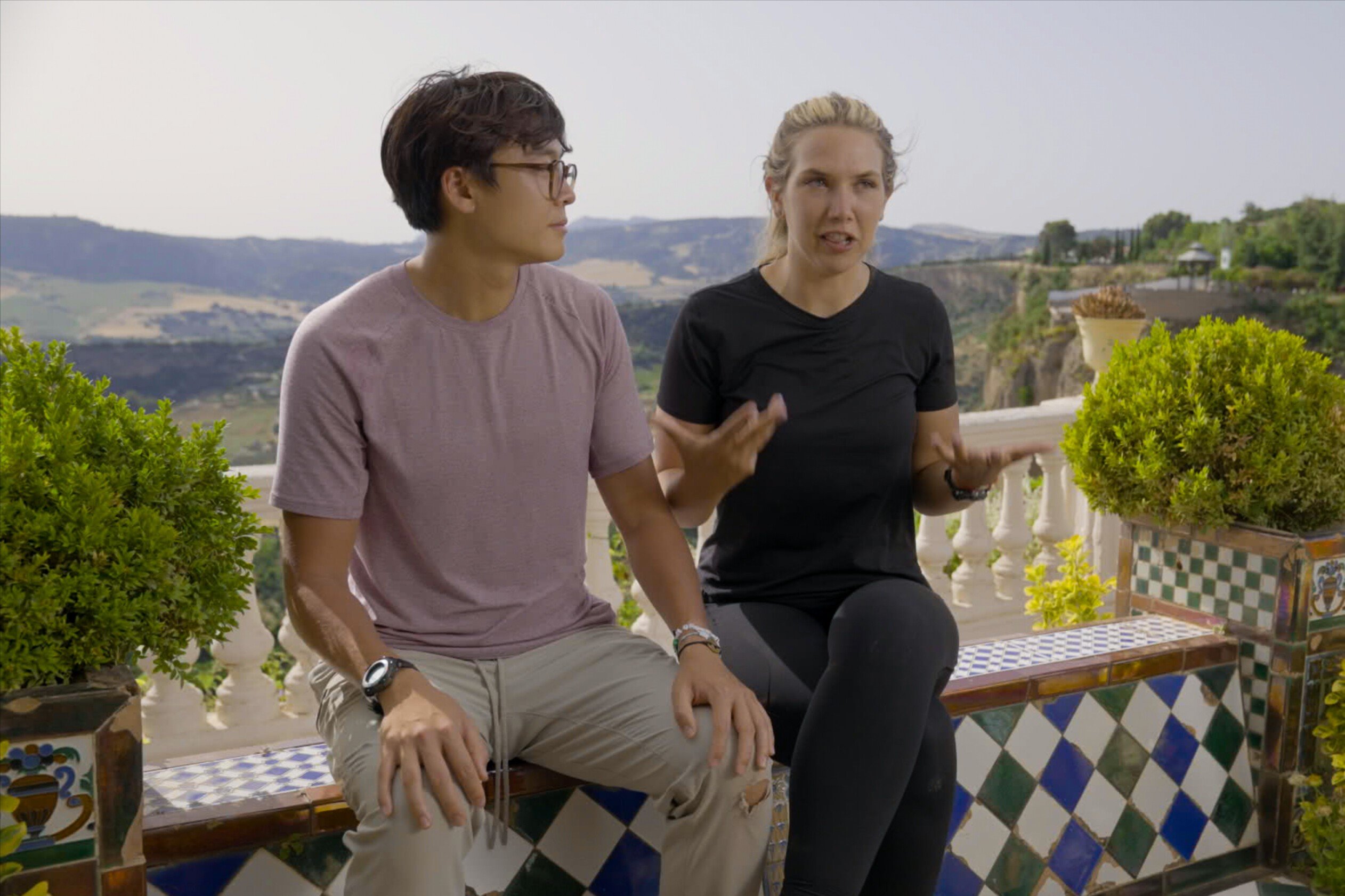 Derek Xiao and Claire Rehfuss, who will compete in 'The Amazing Race 34' Episode 11 on CBS, film a confessional. Derek wears a light purple shirt and tan pants. Claire wears a black shirt and black leggings.