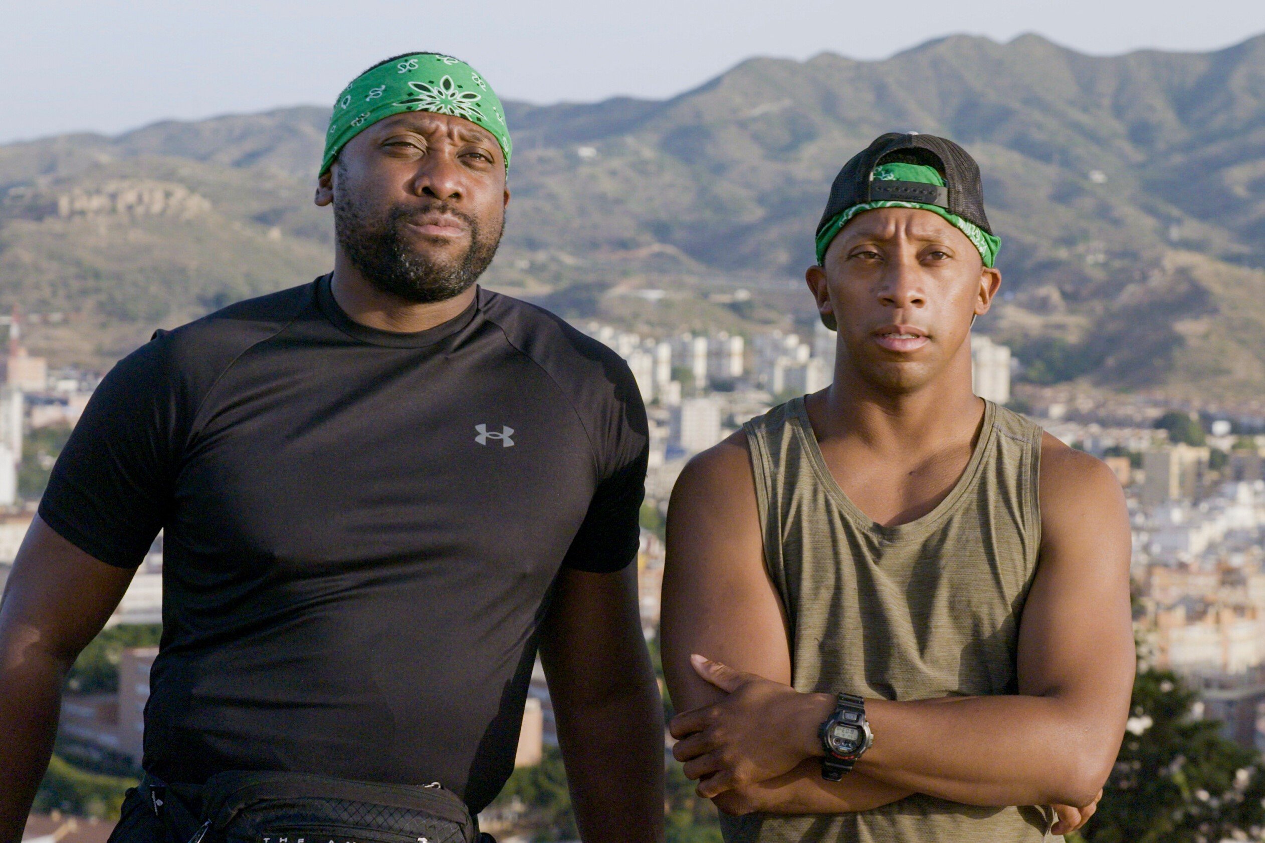 Marcus and Michael Craig, who star in 'The Amazing Race' Season 34 on CBS, film a confessional. Marcus wears a black shirt and green bandana. Michael wears an olive green tank top, green bandana, and black baseball cap backwards.