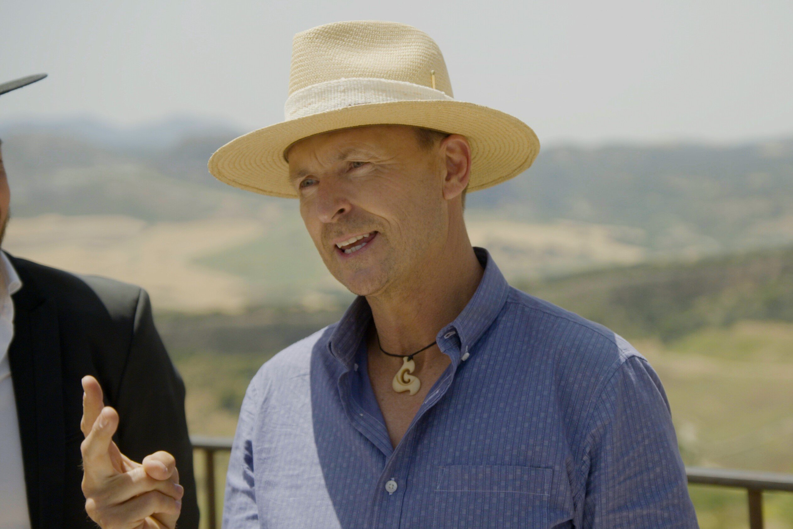 Phil Keoghan, who hosts a new episode of 'The Amazing Race 34' tonight on CBS, wears a blue button-down shirt and tan hat.