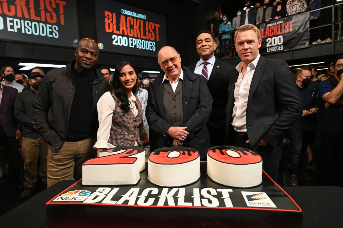 Anya Banerjee attends a celebration for the 200th episode of The Blacklist with other cast members. They stand behind a '200' cake. 