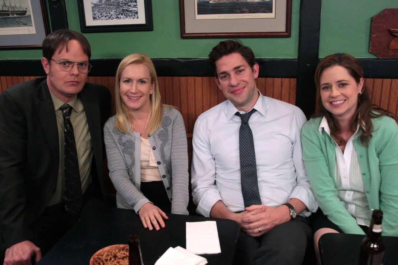 Rainn Wilson as Dwight Schrute, Angela Kinsey as Angela Martin, John Krasinski as Jim Halpert, Jenna Fischer as Pam Beesly Halpert sit next to each other at a restaurant on 'The Office'