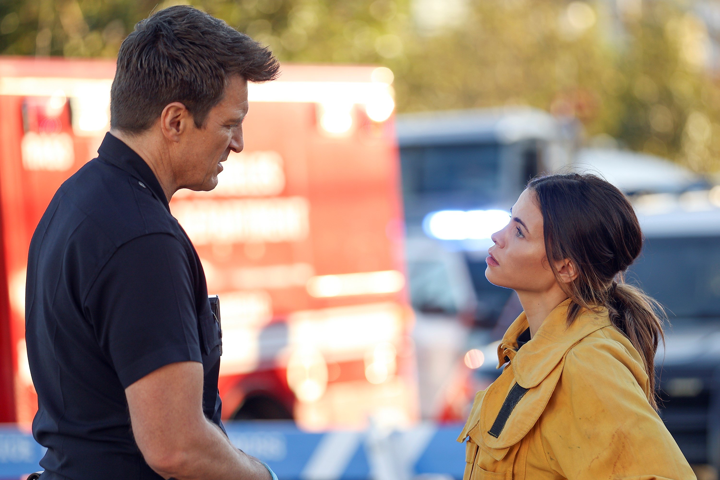 Nathan Fillion as John Nolan and Jenna Dewan as Bailey Nune in 'The Rookie' on ABC. John wears his dark blue police uniform. Bailey wears her yellow firefighter jacket.