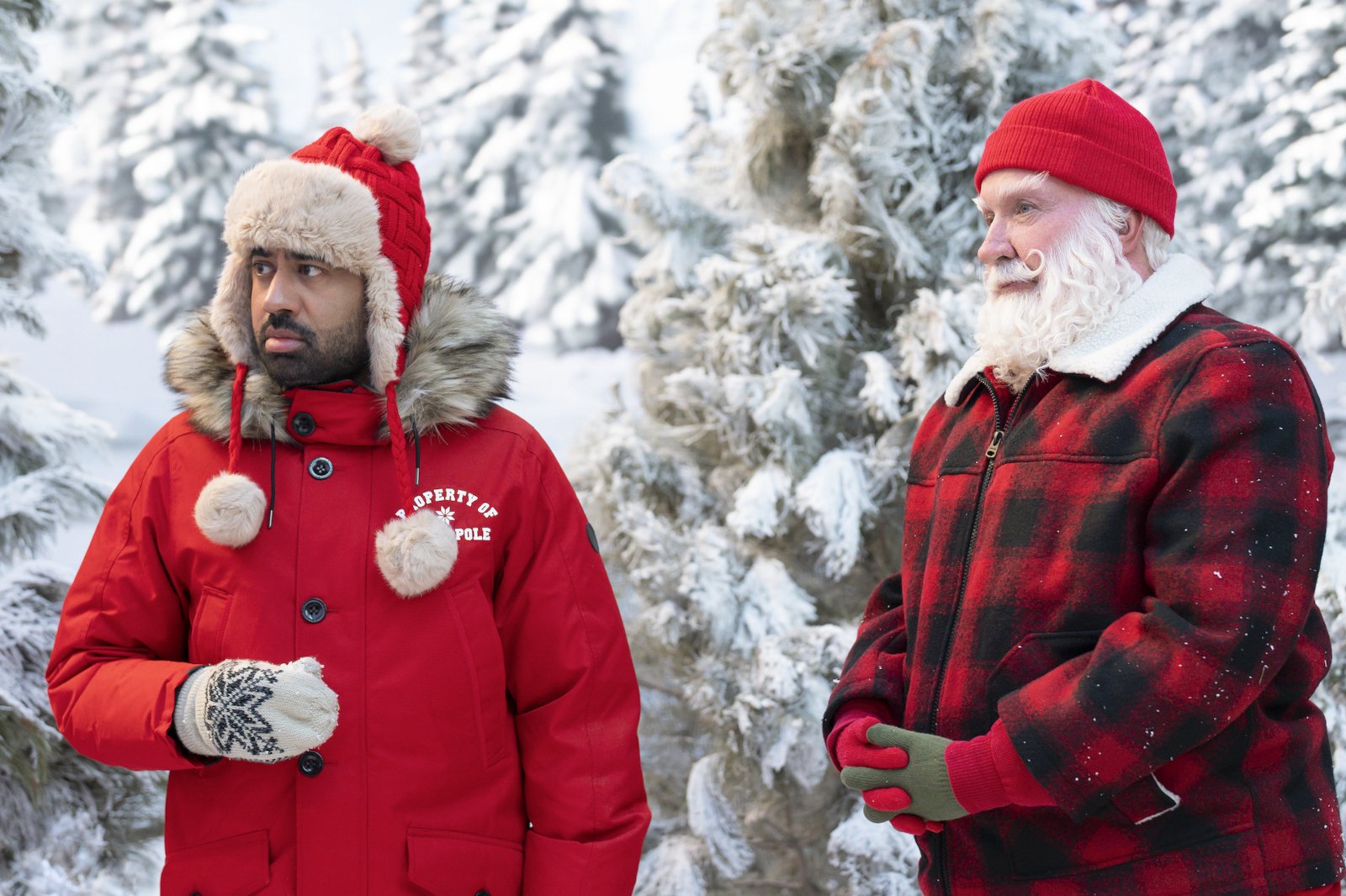 Kal Penn and Tim Allen in 'The Santa Clauses' for our article about episode 4. They're both wearing red coats and standing in the snowy woods.