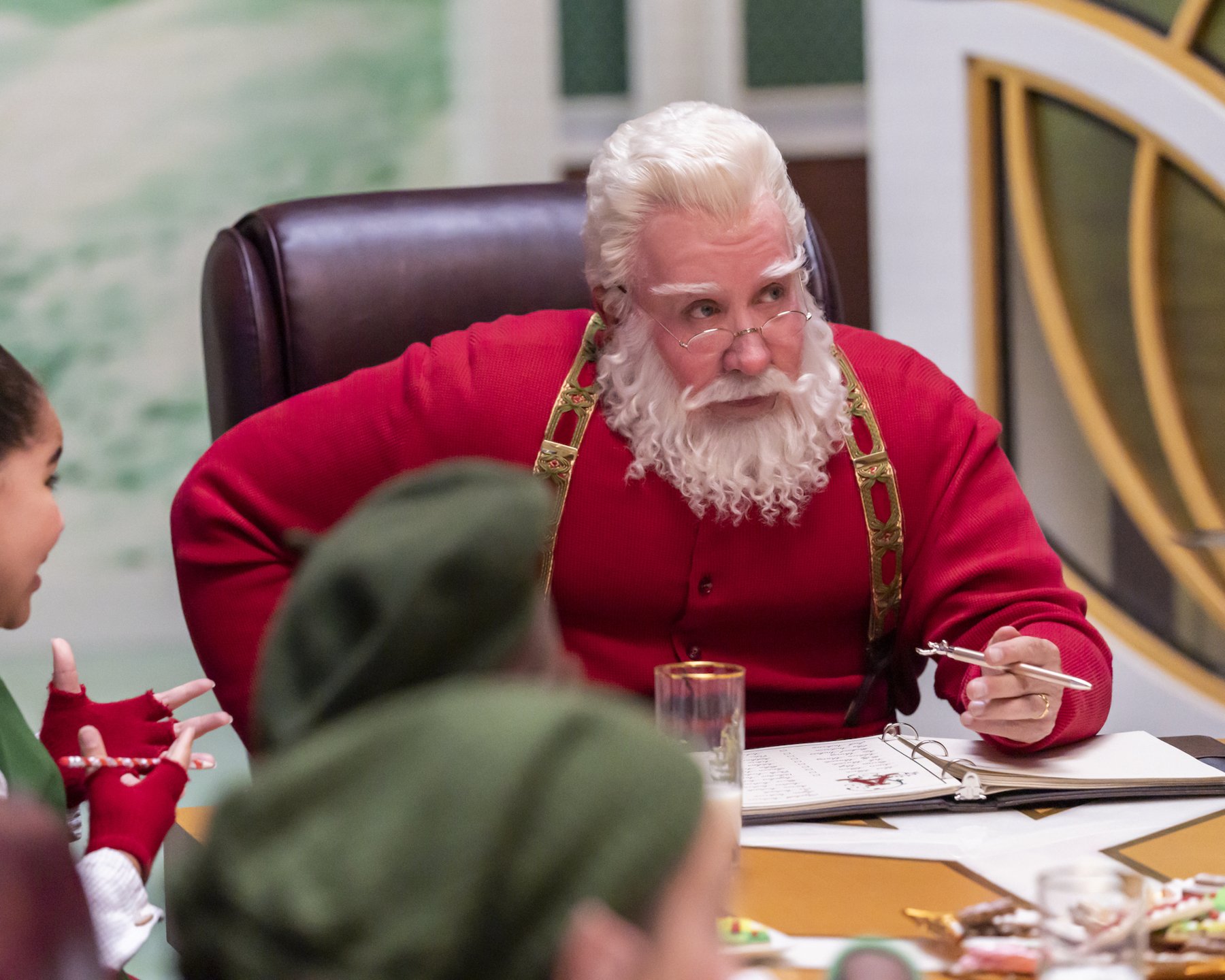 Tim Allen as Scott Calvin/Santa in 'The Santa Clauses.' He's sitting at a table and writing something. His elves are sitting around him.