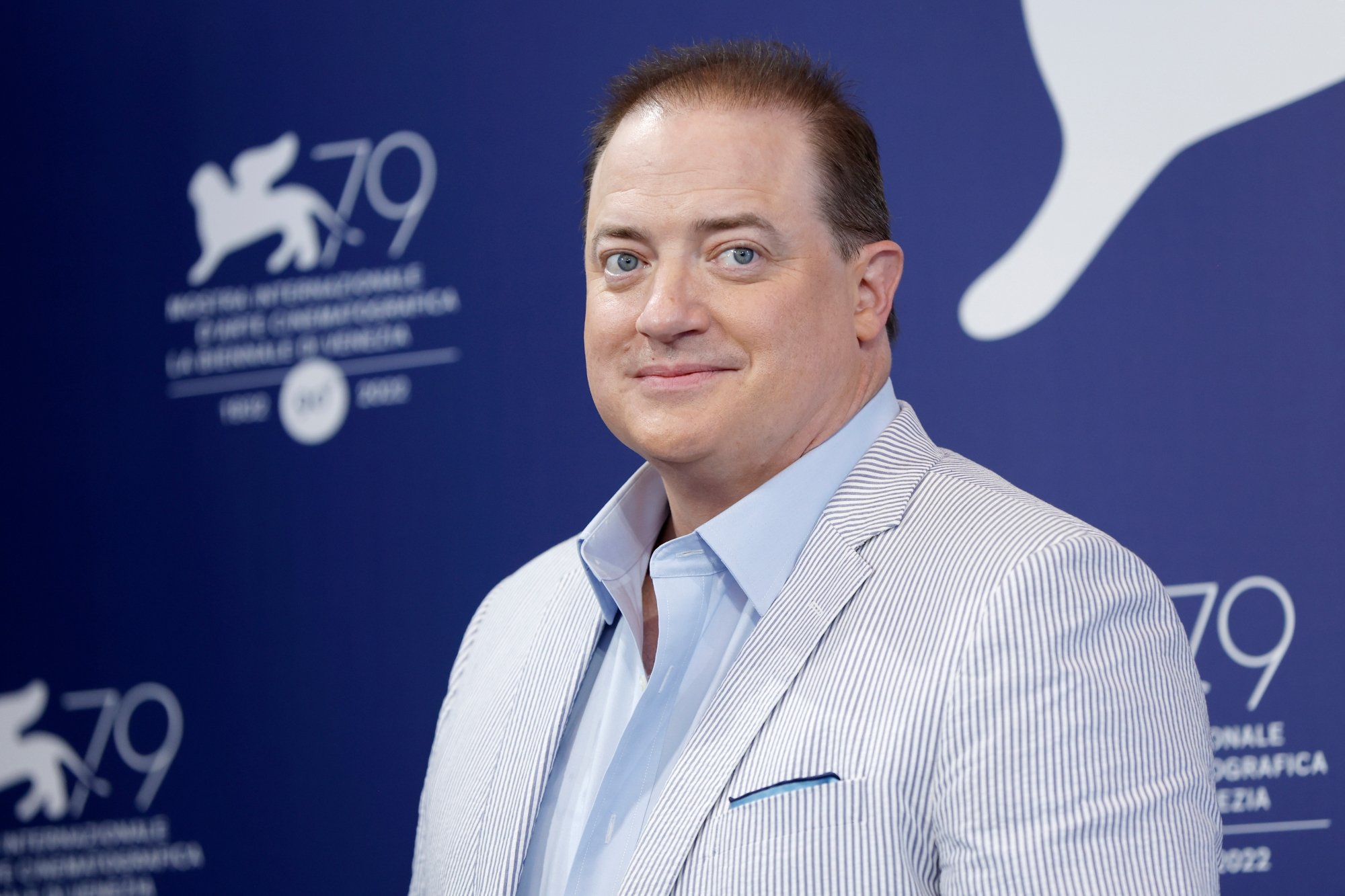 'The Whale' Brendan Fraser with a slight smile on his face, wearing a suit in front of a step and repeat