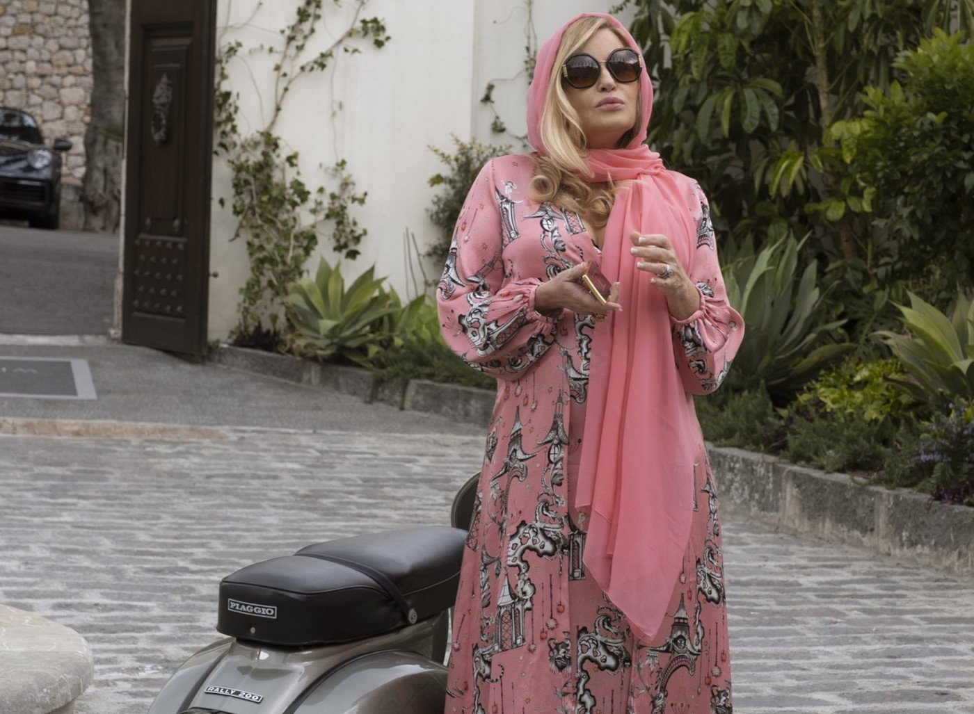 Jennifer Coolidge as Tanya in 'The White Lotus' Season 2. She's wearing a pink dress and shawl and standing in front of a motorbike.