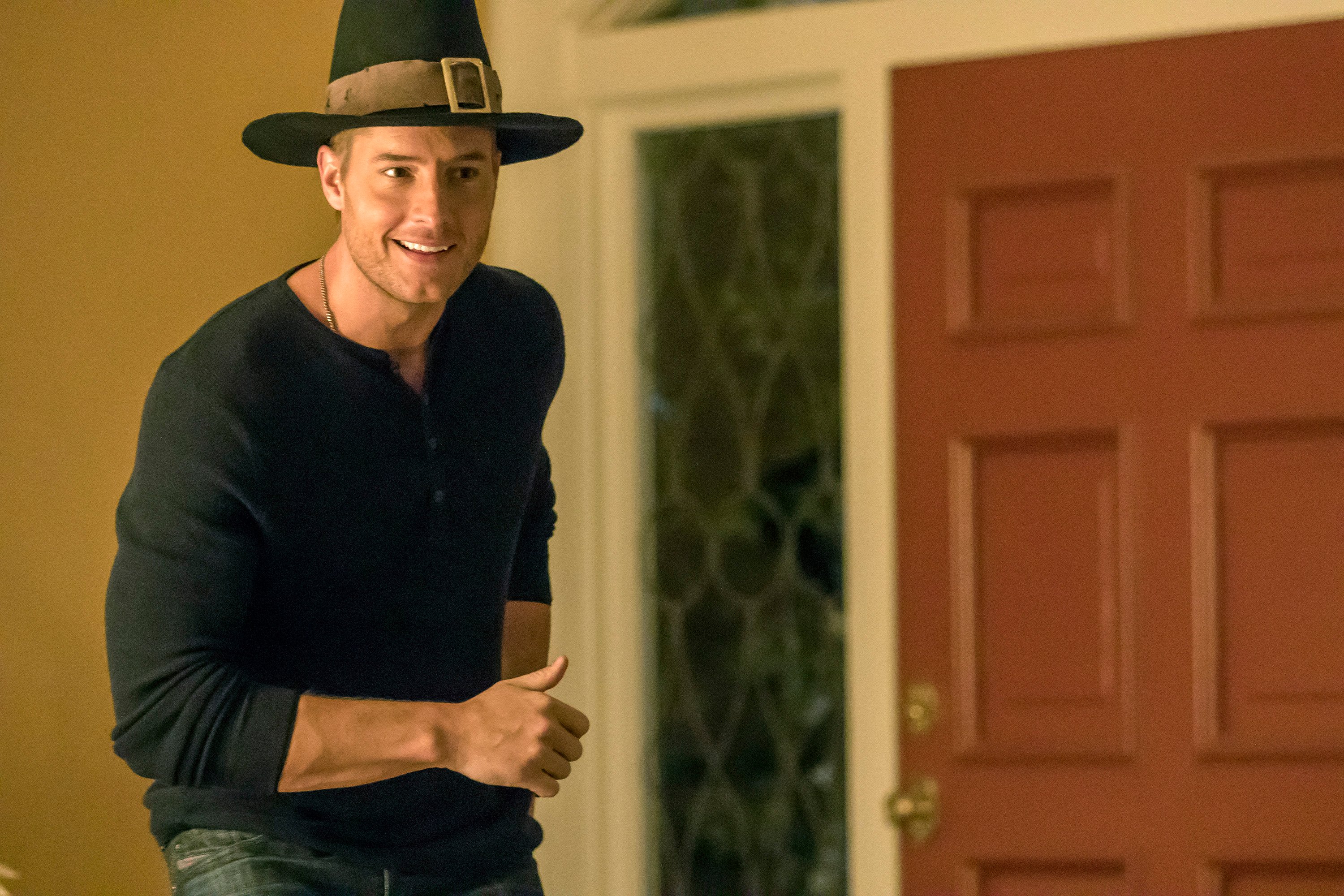 Justin Hartley, in character as Kevin in the Thanksgiving episode of 'This Is Us' Season 1, wears a black Henley shirt, jeans, and the Pilgrim Rick hat.