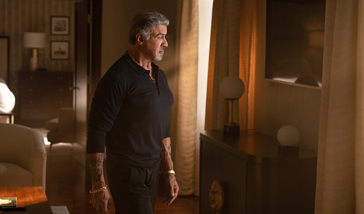 Sylvester Stallone as Dwight Manfredi in Tulsa King. Dwight stands in a bedroom looking glum.