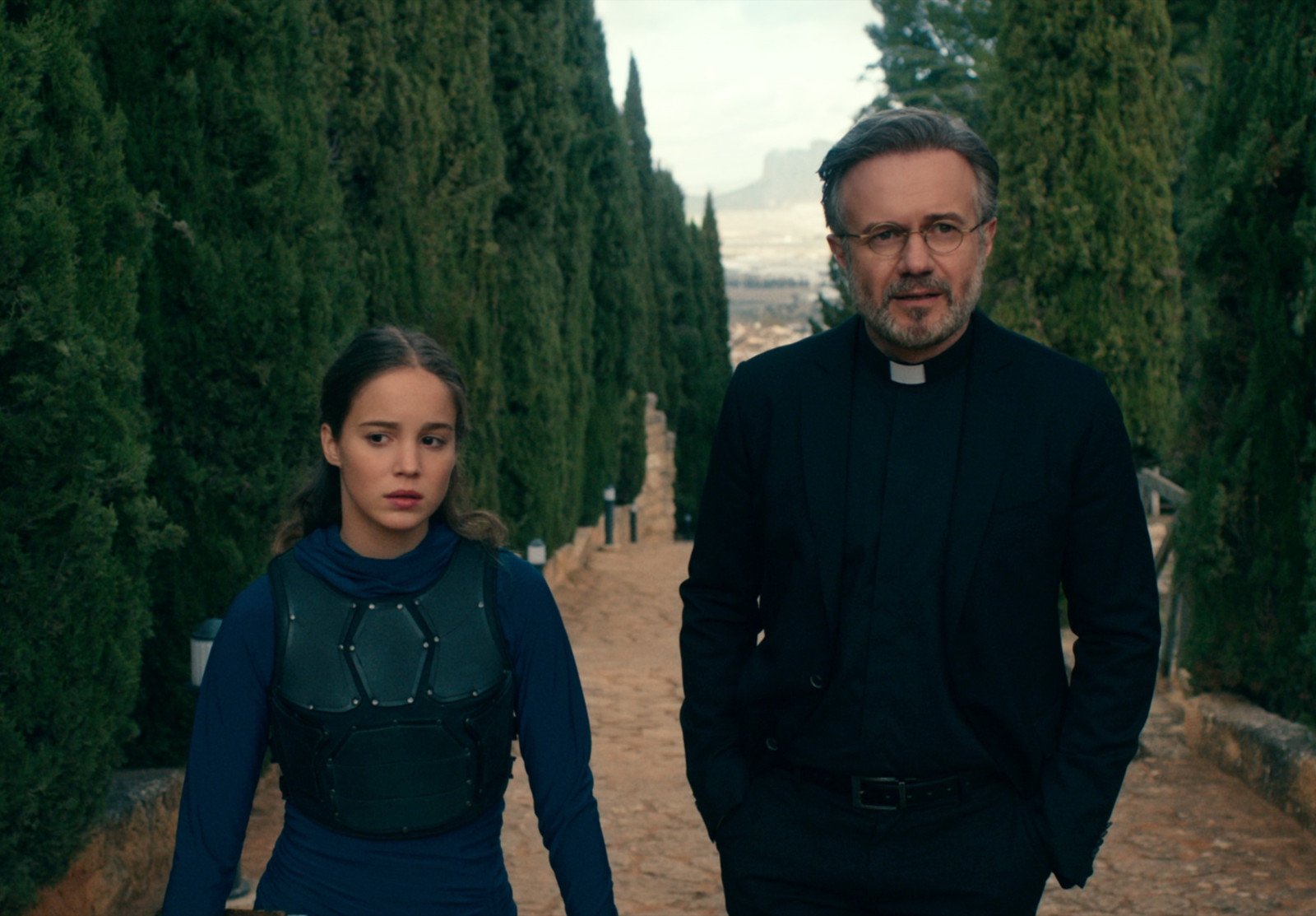 Alba Baptista and Tristán Ulloa in 'Warrior Nun' for our recap of season 1. They're walking side by side and there are trees behind them.