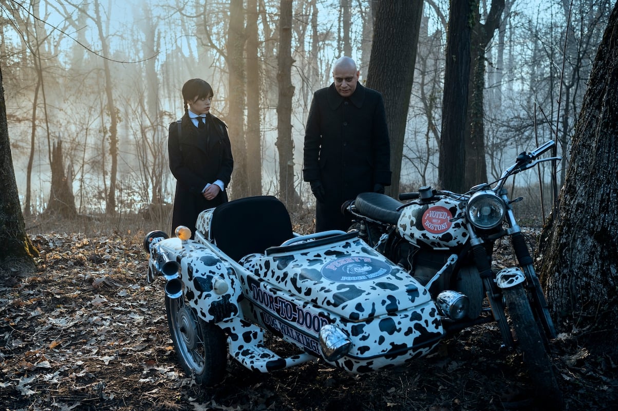 Wednesday and Fester Addams look at a motorcycle in the woods.