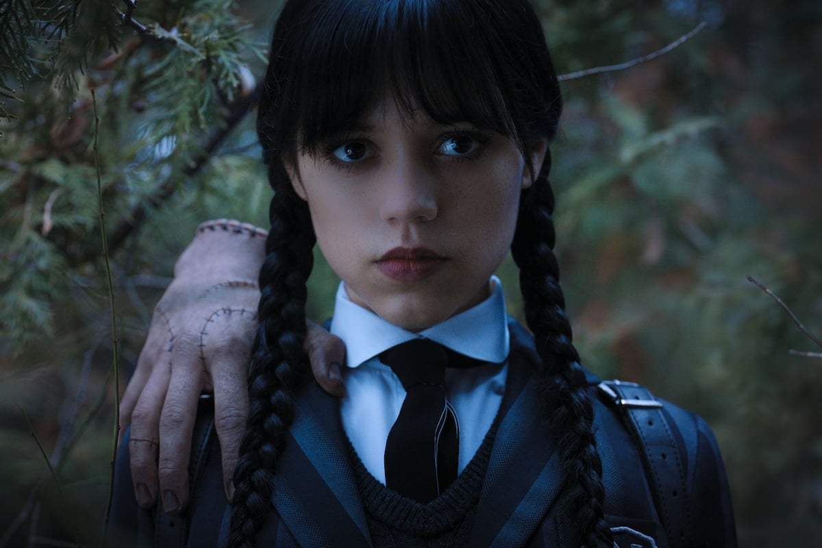 Wednesday Addams (Jenna Ortega) holds Thing on her right shoulder