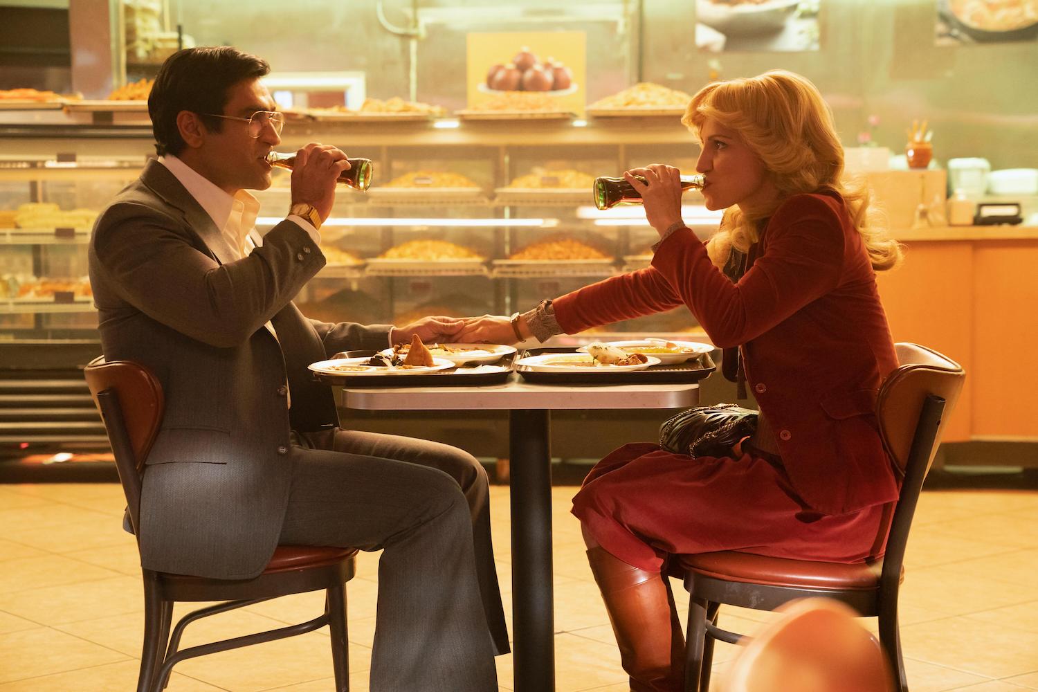 'Welcome to Chippendales' Episode 2 production still of Kumail Nanjiani as Steve Banerjee and Annaleigh Ashford as Irene sitting at a table in a restaurant drinking Coke from bottles.