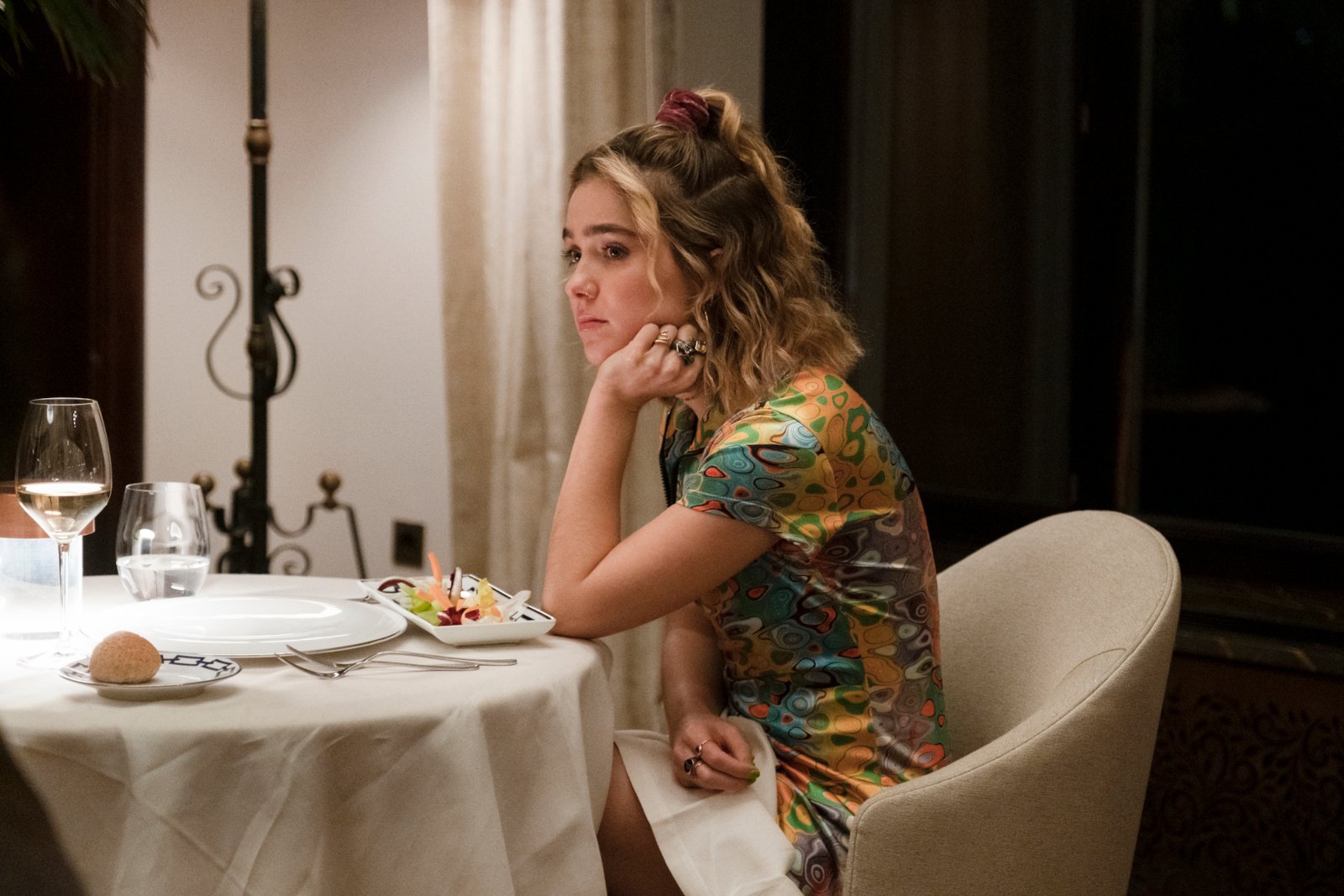 Haley Lu Richardson as Portia in 'The White Lotus' Season 2 for our article about which characters are most likely to die. She's sitting at a table and resting her head on her hand.