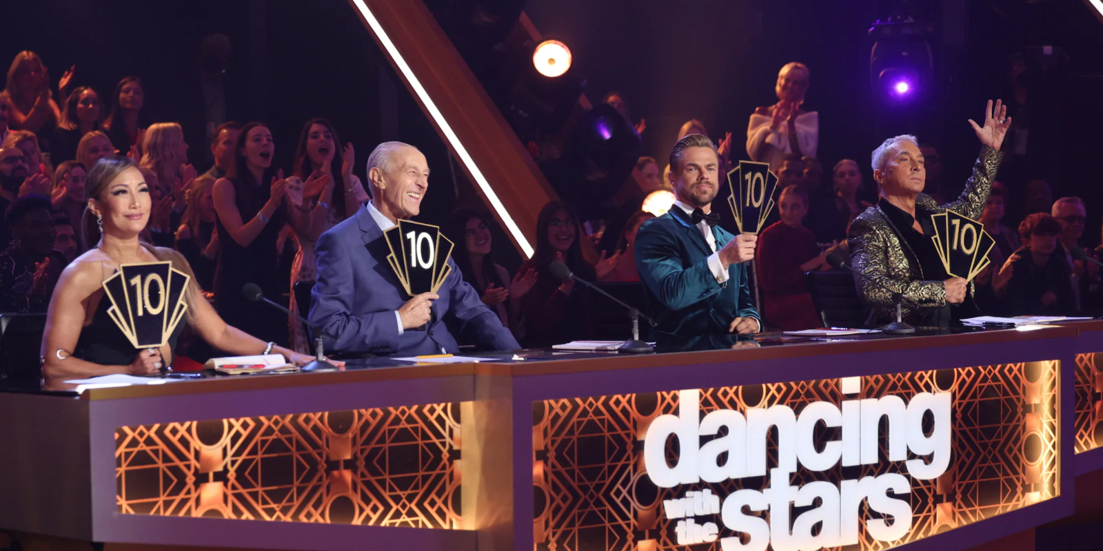 Carrie Ann Inaba, Len Goodman, Derek Hough and Bruno Tonioli seated behind the judges table holding paddles during 'DWTS' season 31 semifinals episode.