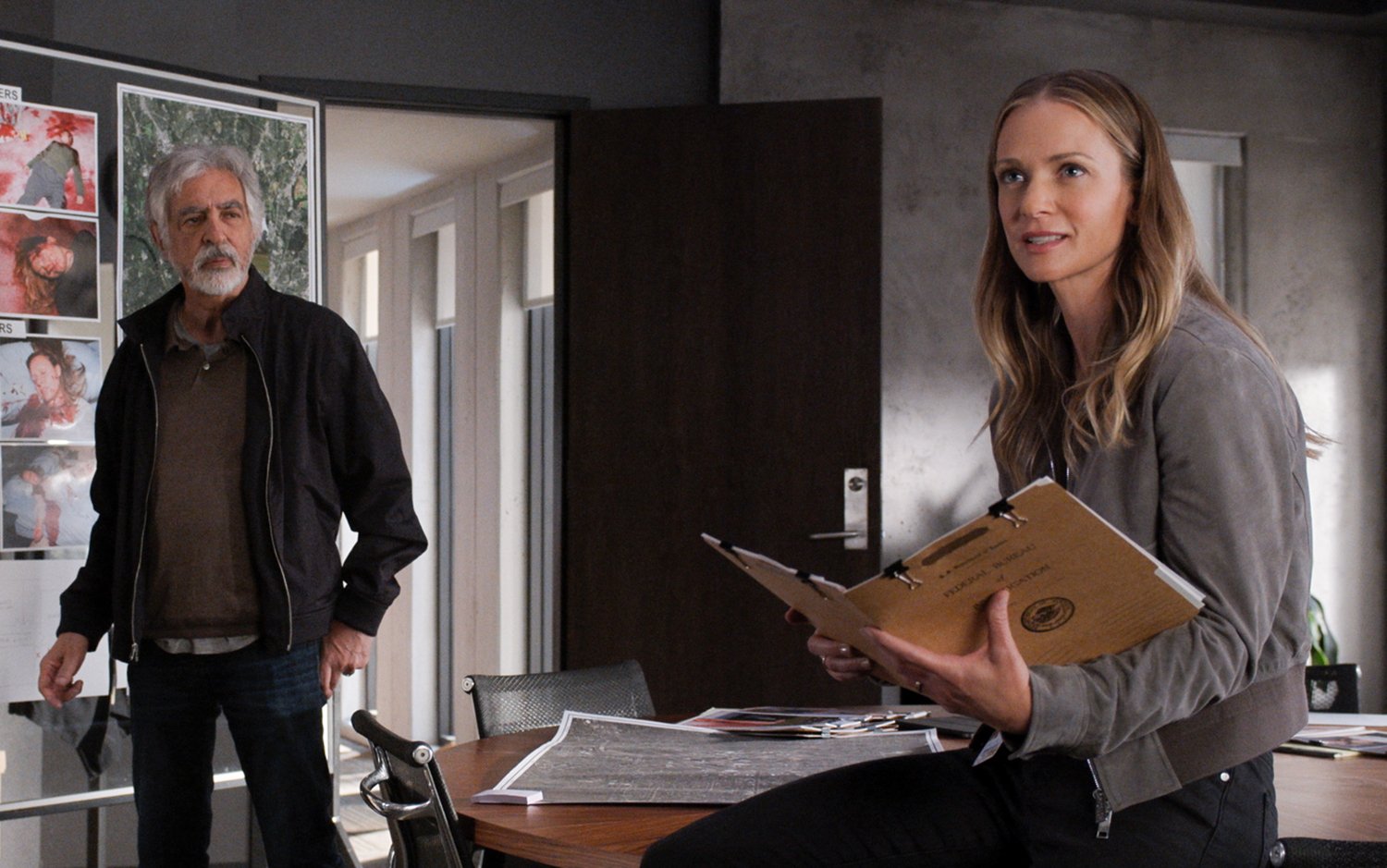 Criminal Minds: Evolution: Joe Mantegna's Dave Rossi stands beside an investigation board as A.J. Cook's Jennifer Jareau sits on a desk holding a folder.