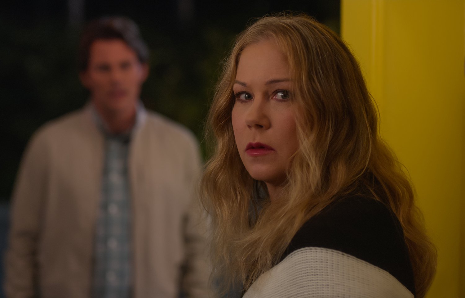 Dead to Me Season 3: James Marsden's Ben Wood stands in the background wearing a plaid shirt and tan jacket as Christina Applegate's Jen Harding looks over her shoulder wearing black
