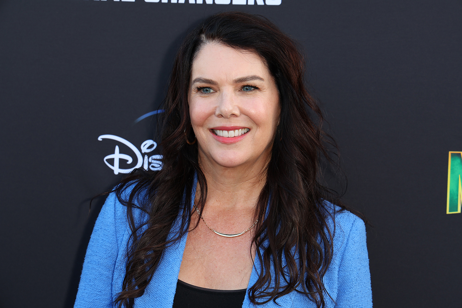 Gilmore Girls star Lauren Graham, who recently shared her theory on Rory's baby, smiles while wearing a black top with a light blue blazer at the The Mighty Ducks Season 2 premiere
