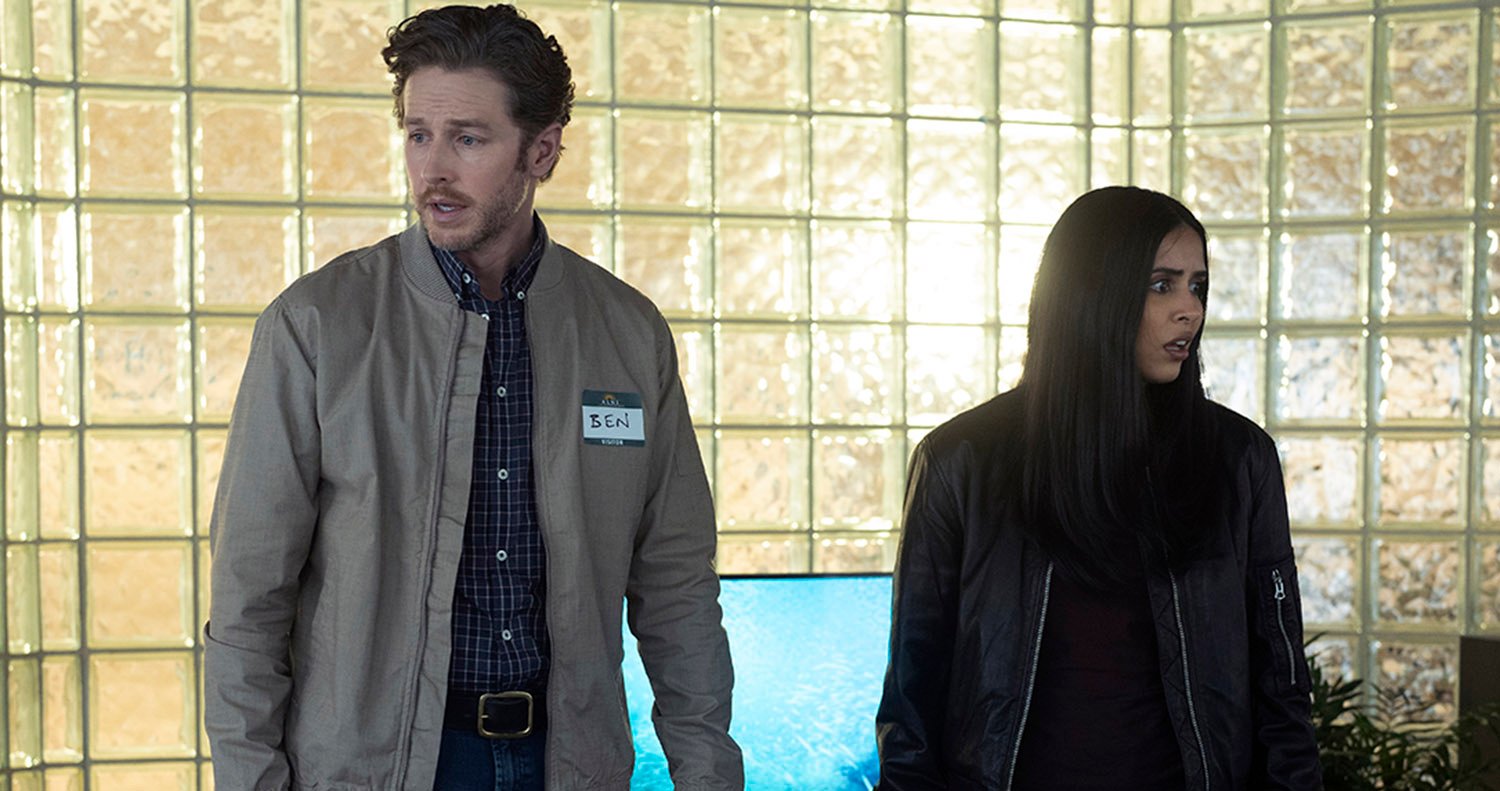 Manifest Season 4: Josh Dallas as Ben Stone, wearing a plaid shirt and jacket, stands beside Parveen Kaur as Saanvi Bahl, wearing all black, as they look in opposite directions.
