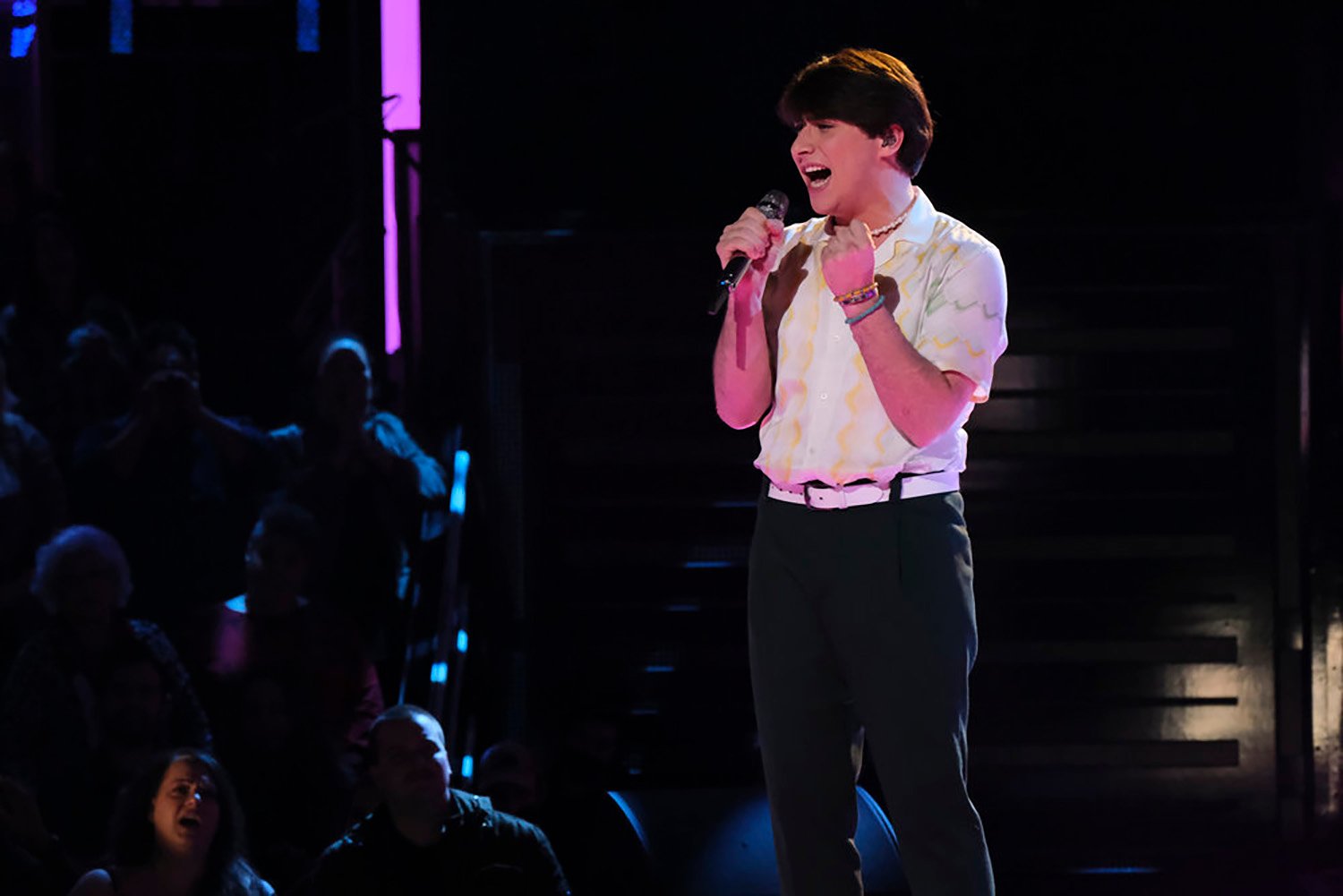 Kique performs on The Voice wearing black pants and a cream-colored button-down one week before testing positive for COVID.
