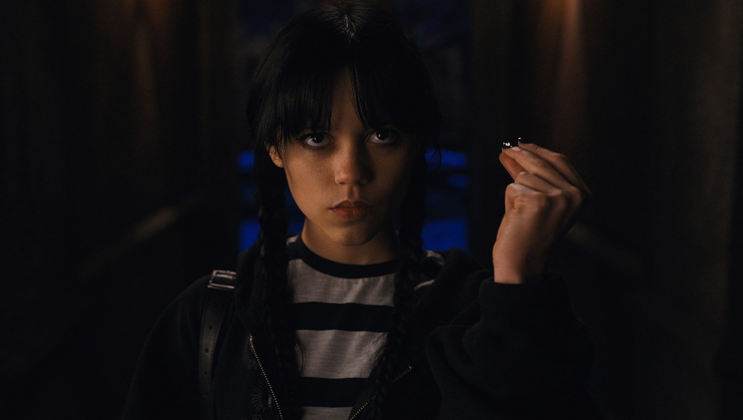 Wednesday Season 1 loose ends: A close-up shot of Jenna Ortega as Wednesday Addams snapping her fingers while wearing a white and black striped top.