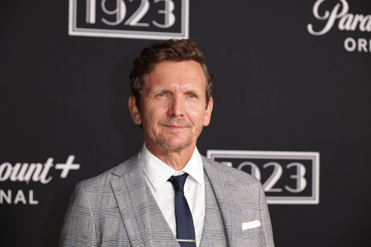 Sebastian Roché plays Father Renaud in '1923.' Roché attends the 1923 premiere wearing a grey suit, white collared shirt, and dark blue tie. 