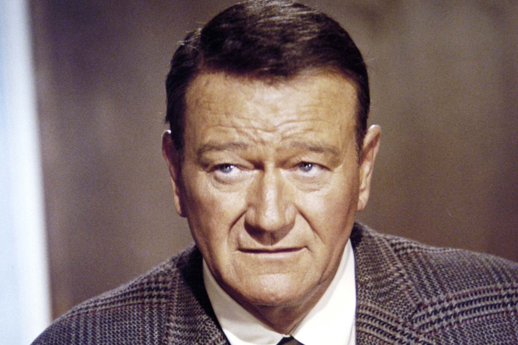 Acting legend John Wayne wearing a suit and tie with a plain look on his face