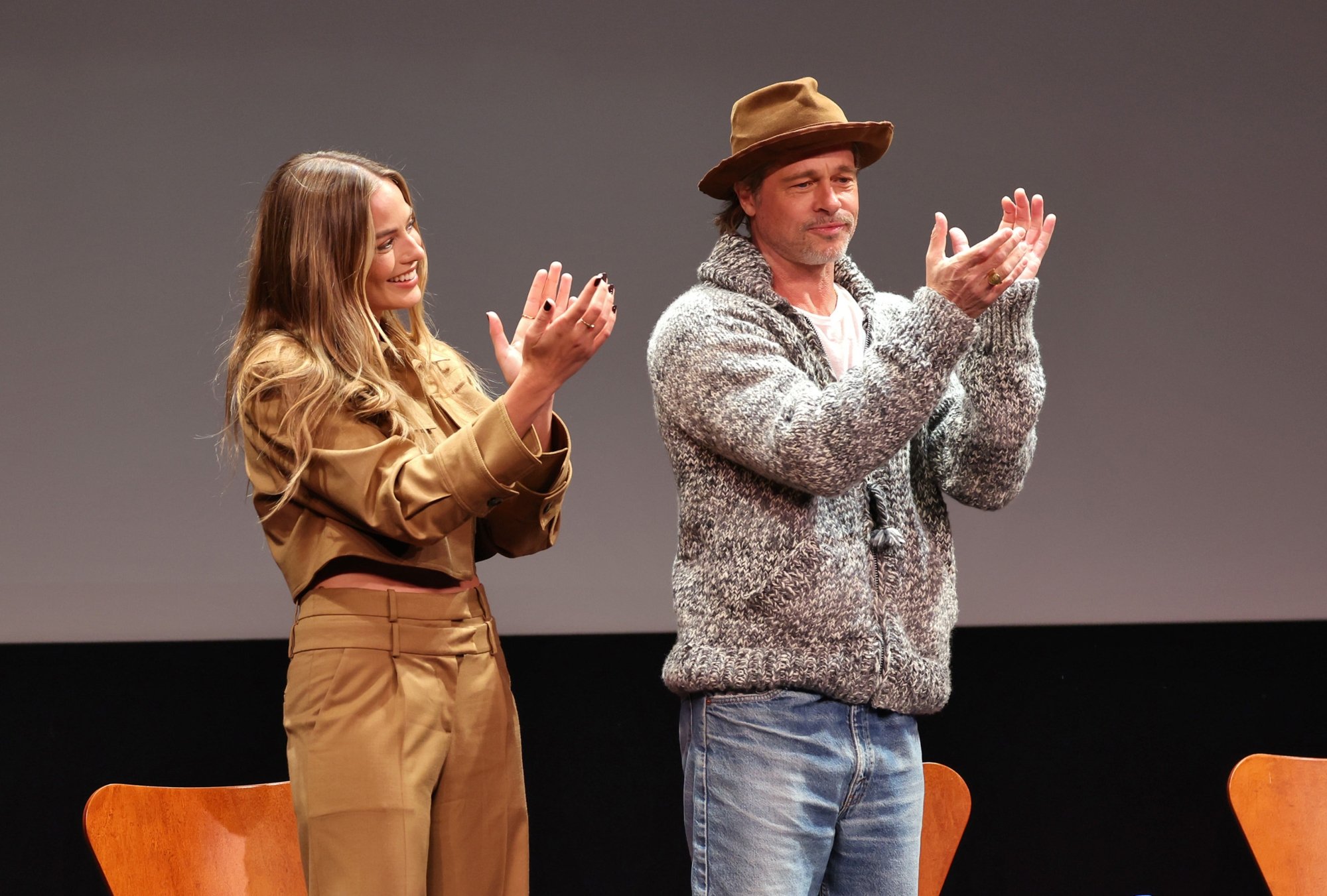 'Babylon' actors Margot Robbie and Brad Pitt clapping and smiling as they stand up from their chairs at a screening