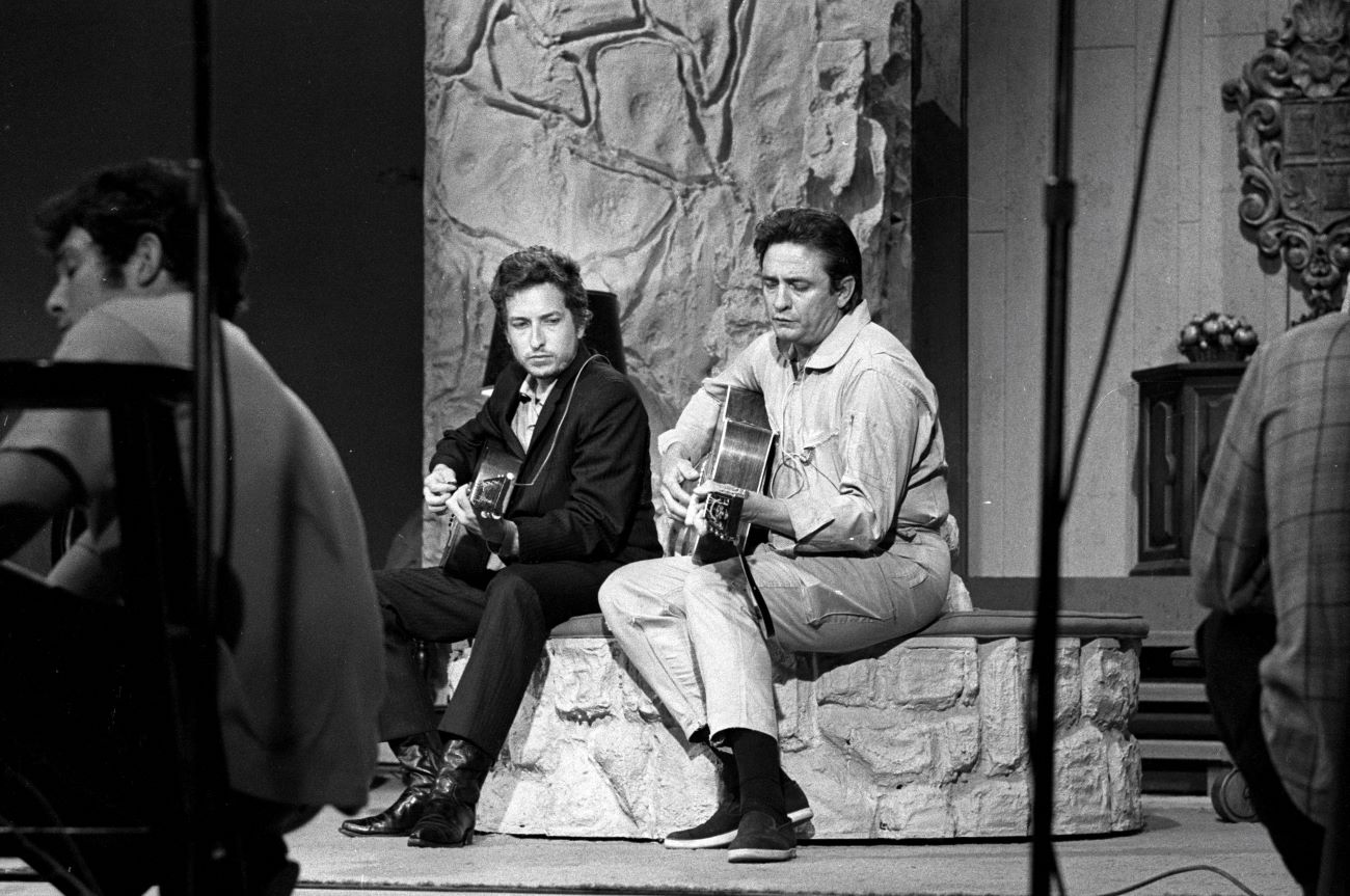 A black and white picture of Bob Dylan and Johnny Cash sitting on a step with guitars.