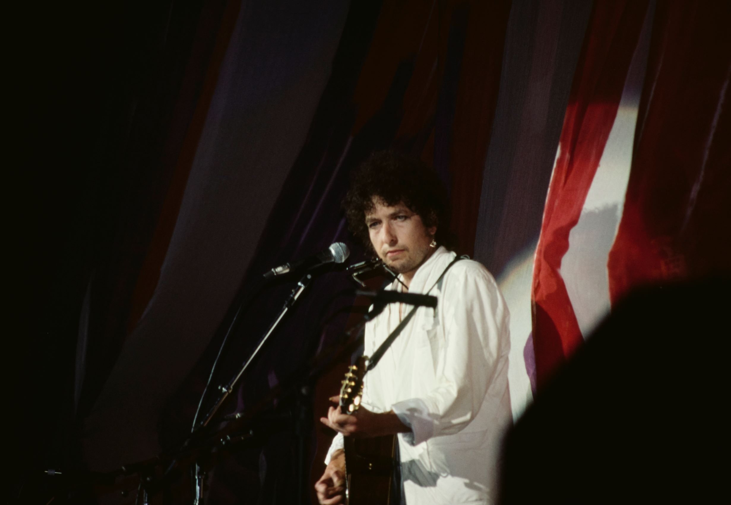 Bob Dylan wears a white suit and holds a guitar onstage at Live Aid.
