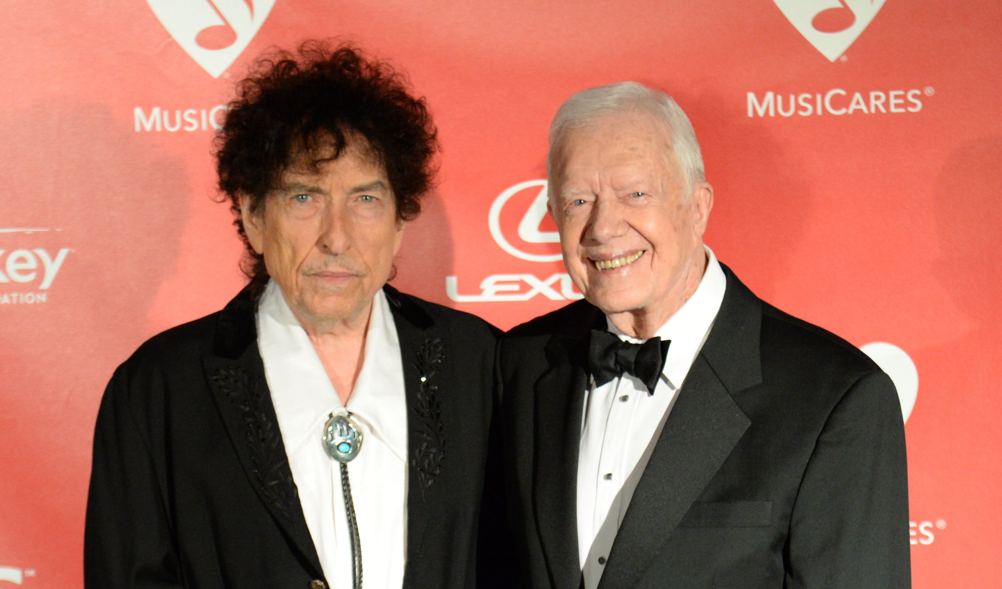 Bob Dylan and Jimmy Carter wear black and stand in front of a red background.