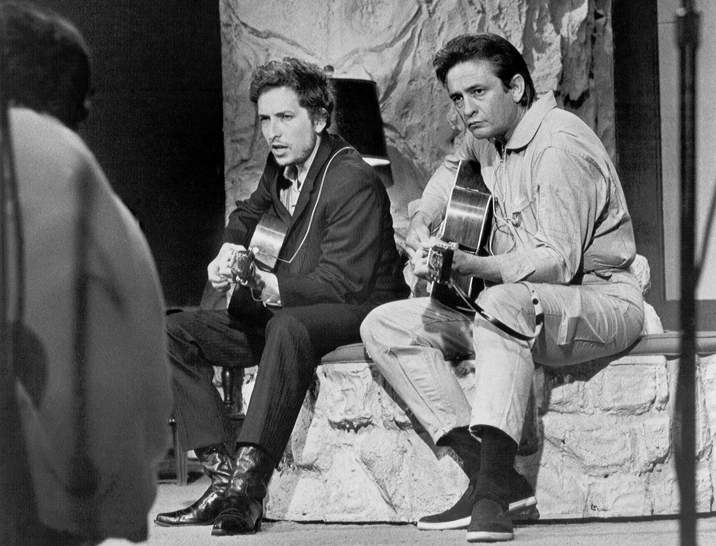A black and white picture of Bob Dylan and Johnny Cash sitting on a stone step with guitars.