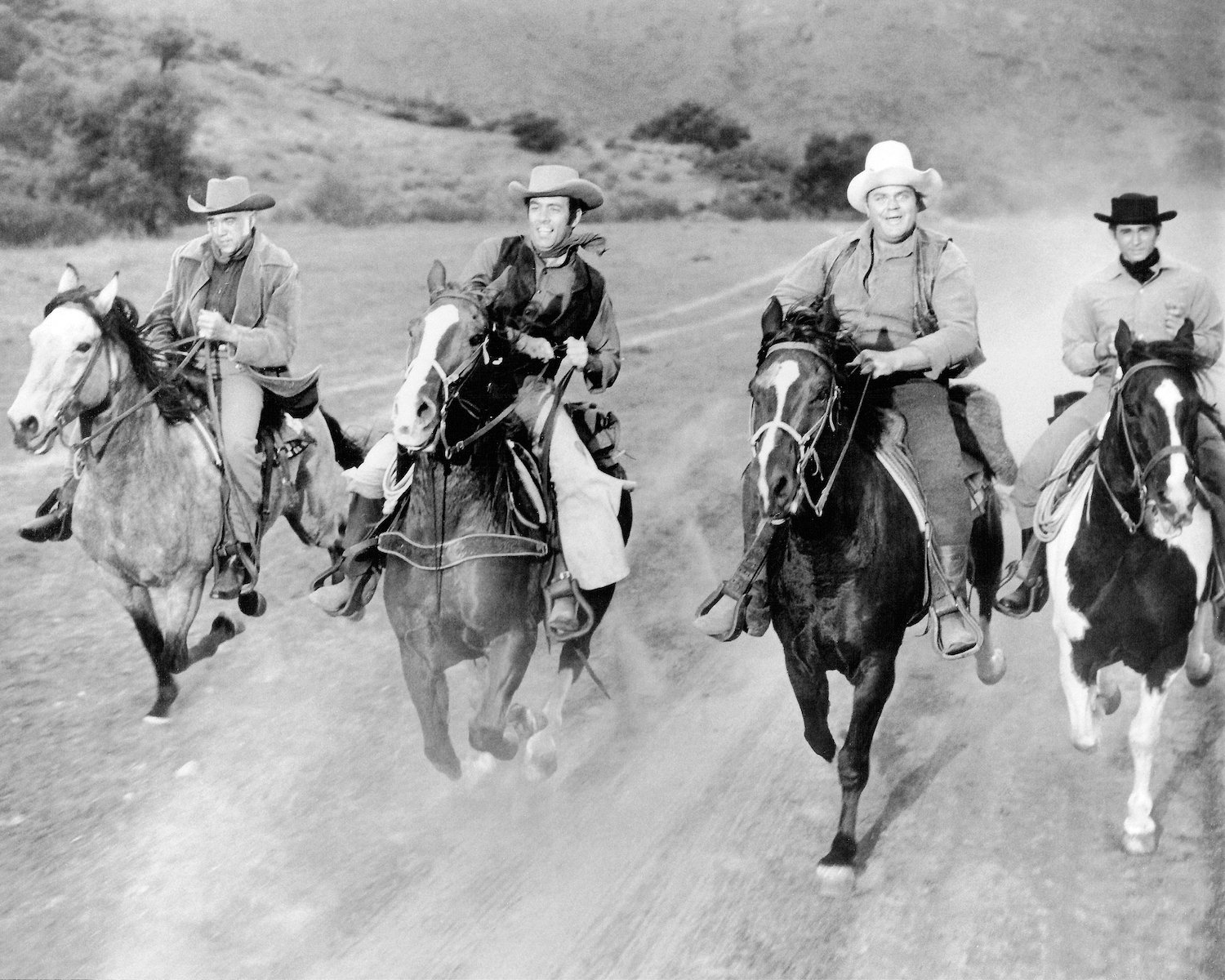 A black and white photo of Lorne Greene, Pernell Roberts, Dan Blocker, and Michael Landon riding horses in 'Bonanza'