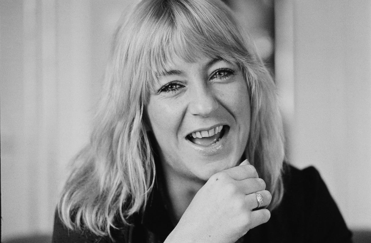 A black and white portrait of Christine McVie smiling.