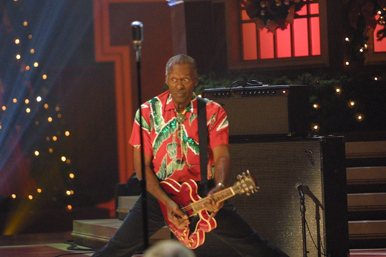 Christmas song artist Chuck Berry wearing a red and green shirt while playing guitar on stage.
