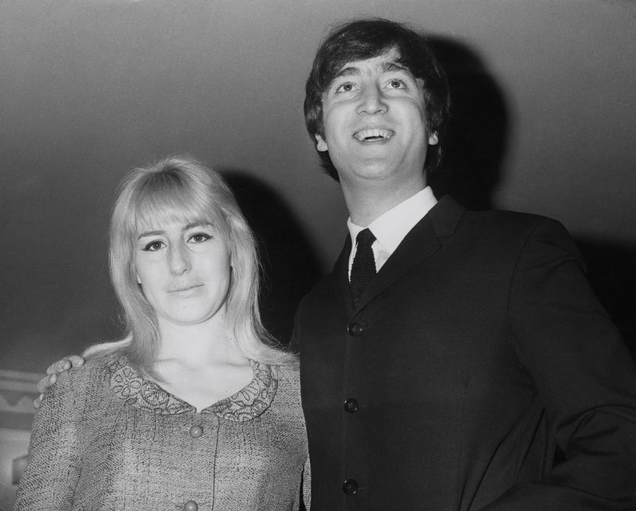 A black and white picture of John Lennon standing with his arm around Cynthia Lennon's shoulders.
