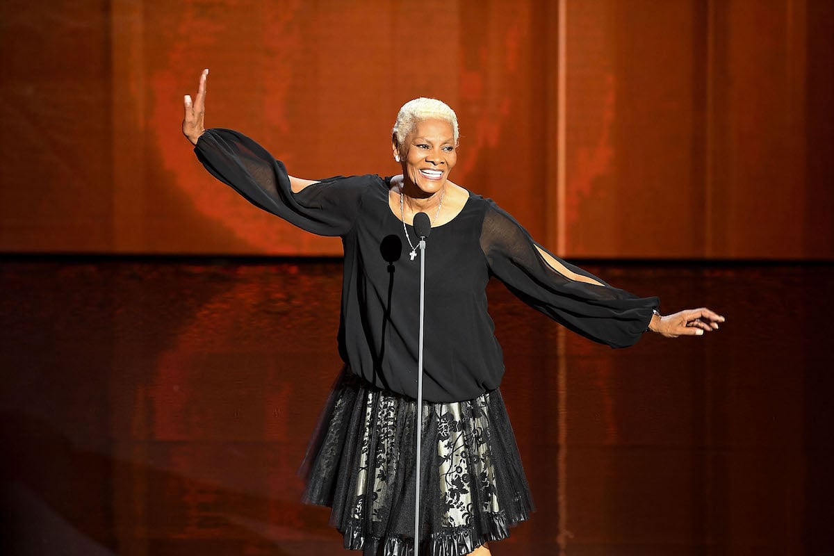 Dionne Warwick, a nominee for the 2022 Showbiz Social Media Awards, smiles and looks on standing in front of a microphone
