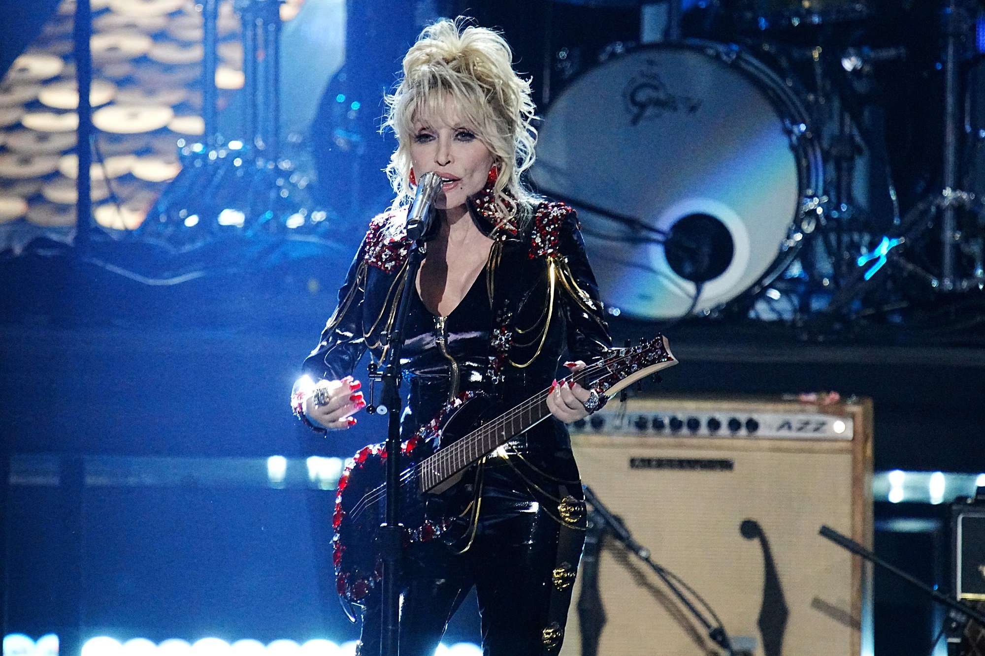 Dolly Parton performs onstage in a black leather outfit with a black guitar