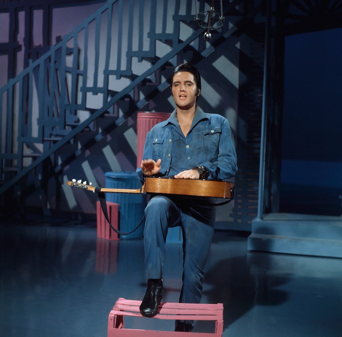 Elvis Presley sits with a guitar on his lap