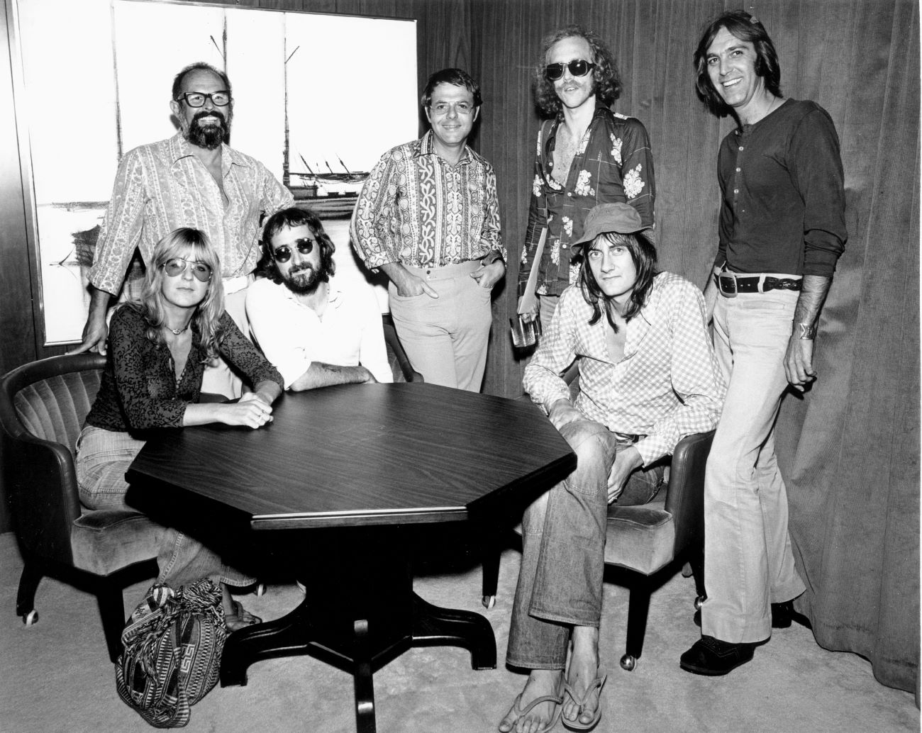 A black and white picture of the 1970-era members of Fleetwood Mac sitting around a table.