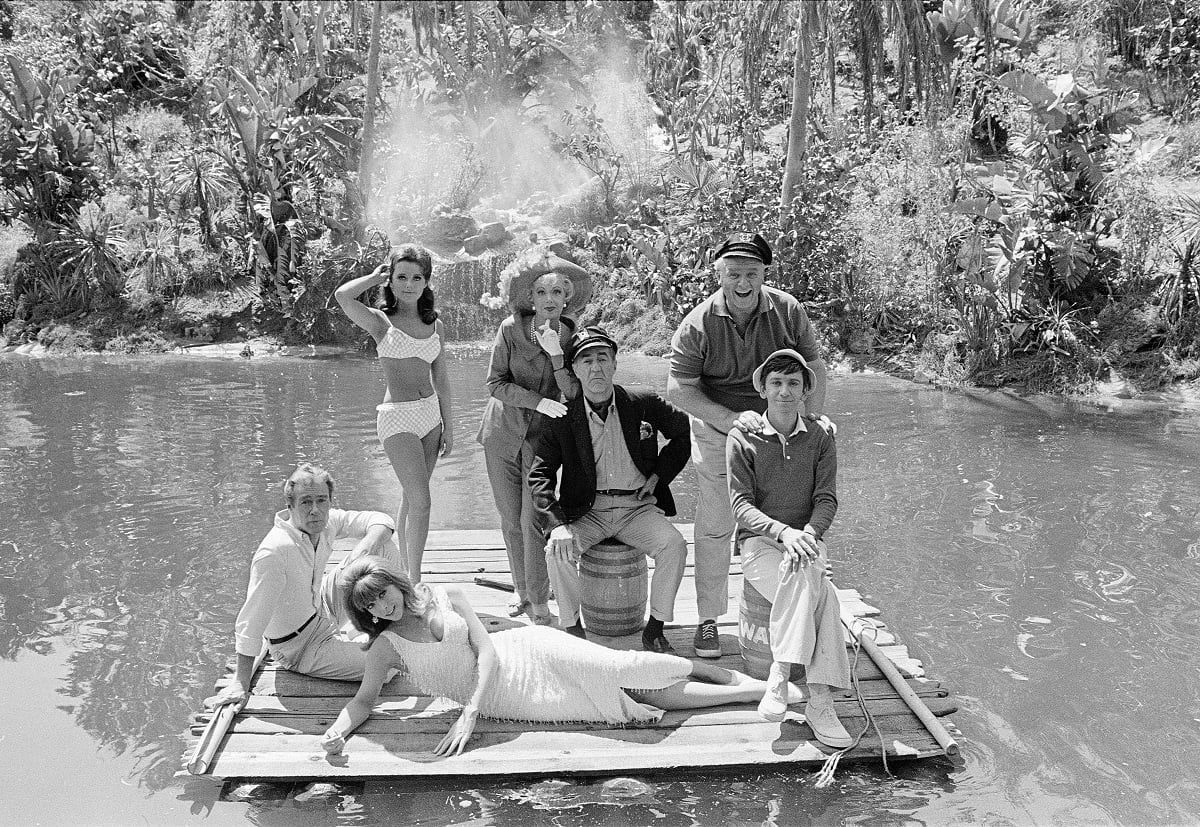 A black and white photo of the 'Gilligan's Island' cast posing on a wooden raft in a lagoon.