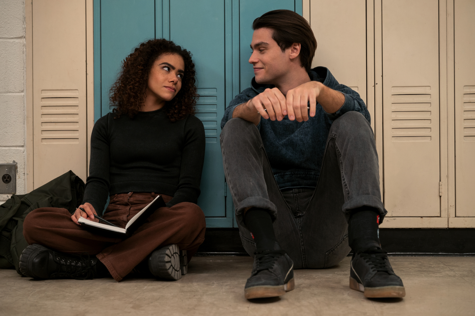 Antonia Gentry as Ginny and Felix Mallard as Marcus Baker in 'Ginny and Georgia' Season 2 for our article about its release date, cast, and trailer. The pair are leaning against their lockers and looking at one another.