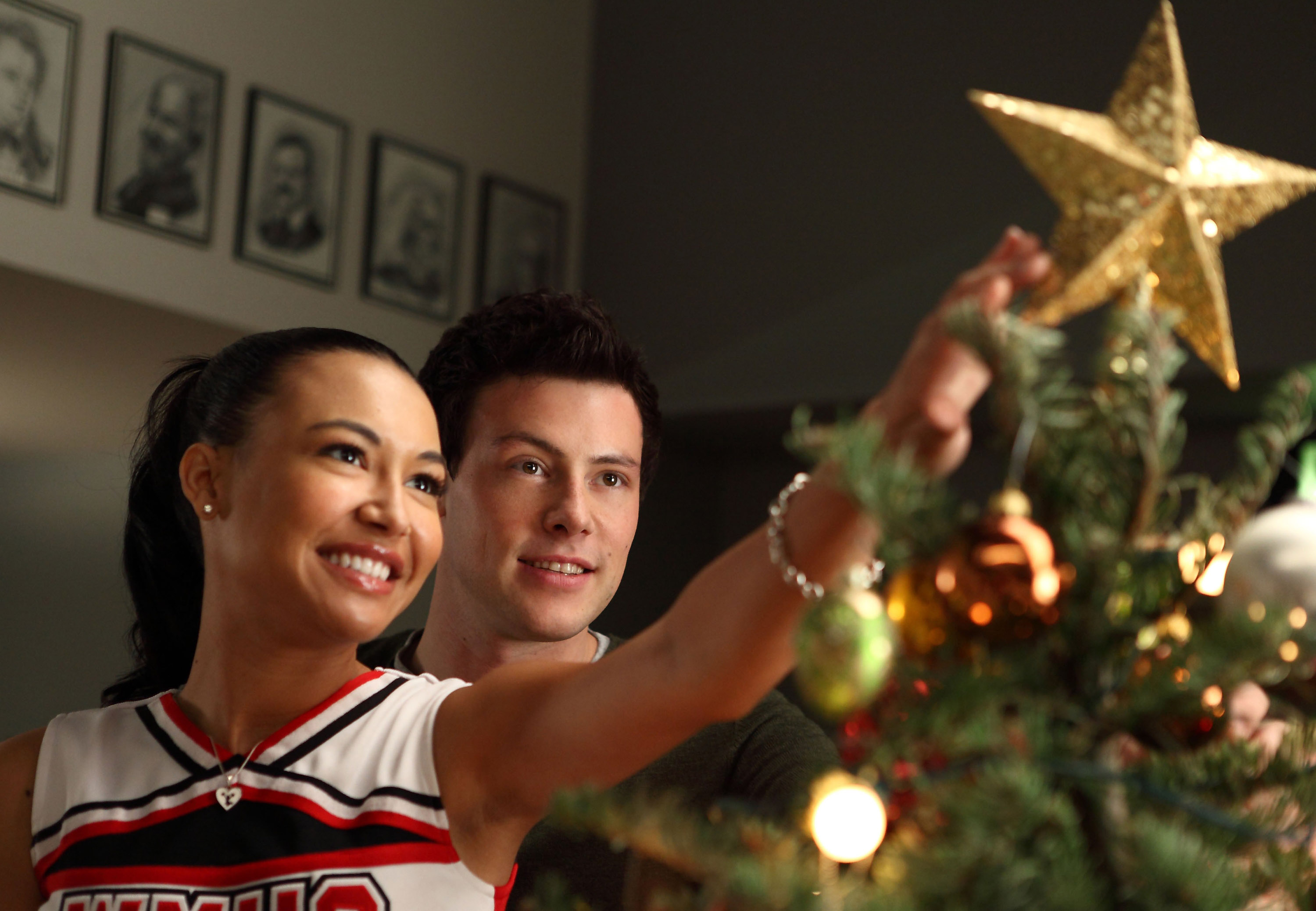 Naya Rivera as Santana Lopez and Cory Monteith as Finn Hudson in 'Glee' Season 2 Episode 10, 'A Very Glee Christmas.' Santana wears her red, black, and white cheerleading uniform. Finn wears a dark green sweater.