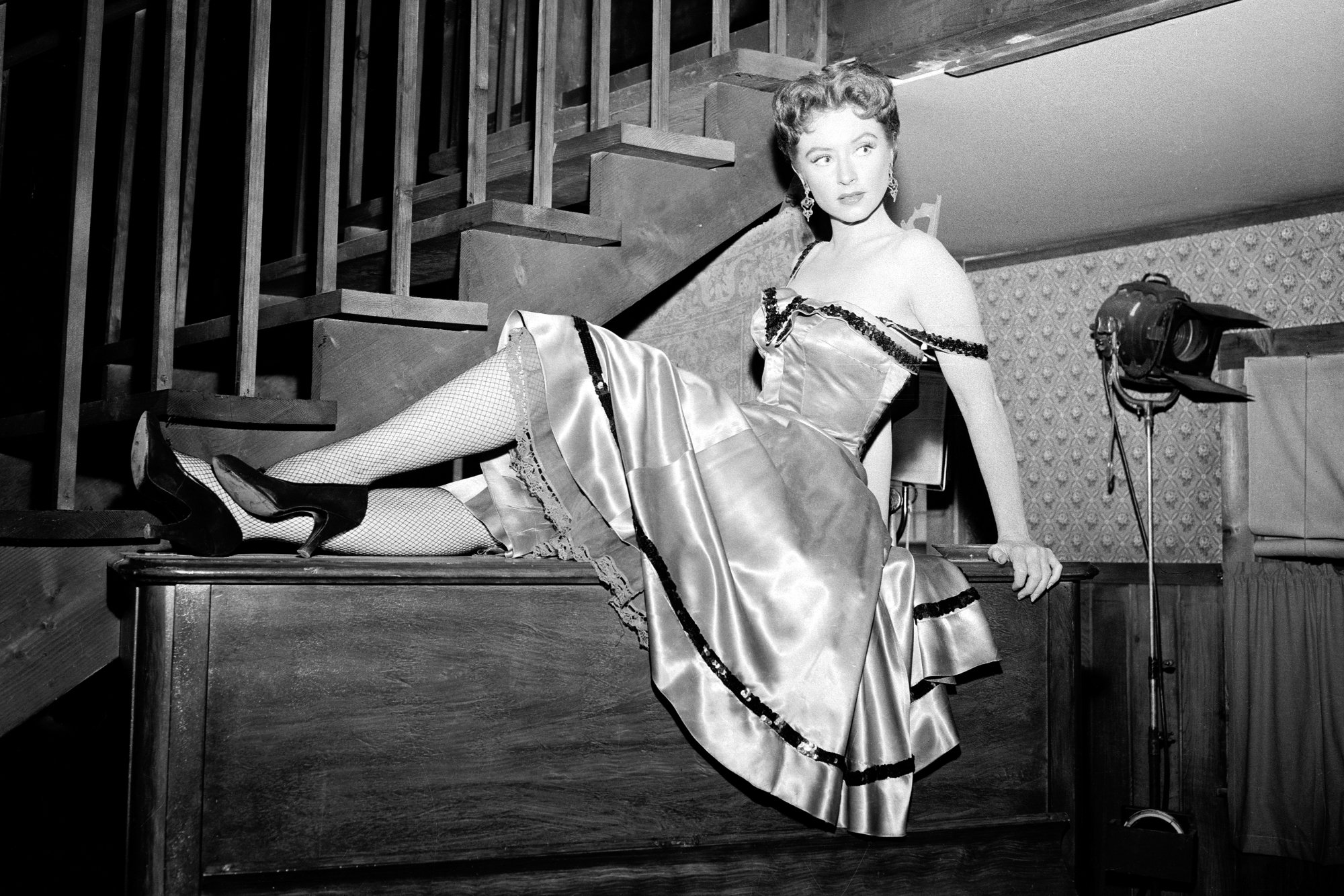 'Gunsmoke' Amanda Blake as Miss Kitty Russell in a black-and-white picture leaning back on the top of a piano in front of a staircase