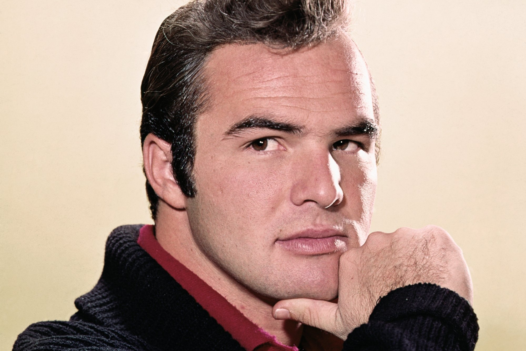 'Gunsmoke' Burt Reynolds holding his thumb under his chin in front of a blank background