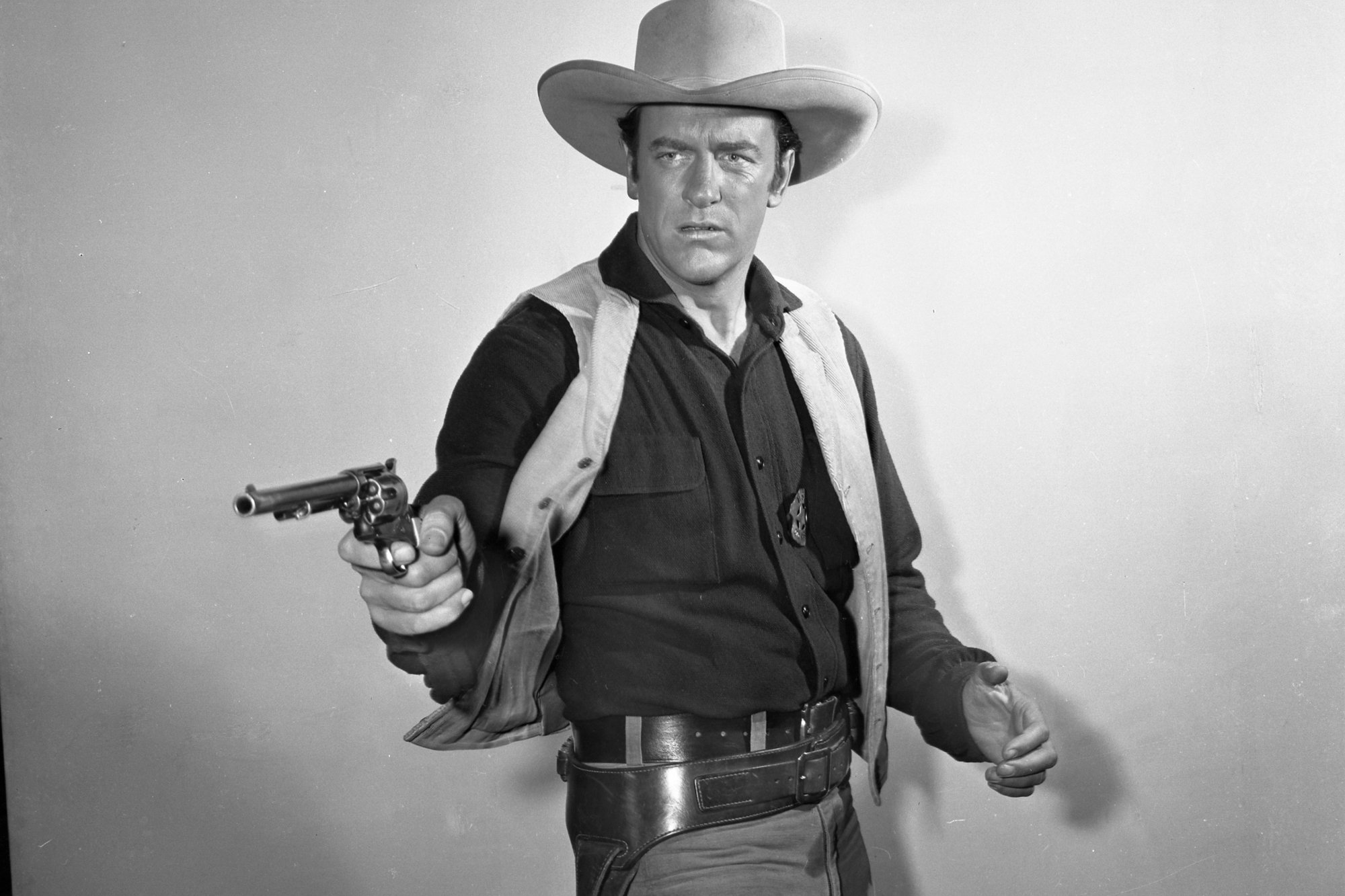 'Gunsmoke' James Arness as Matt Dillon in a black-and-white picture in his Western uniform, holding out his gun